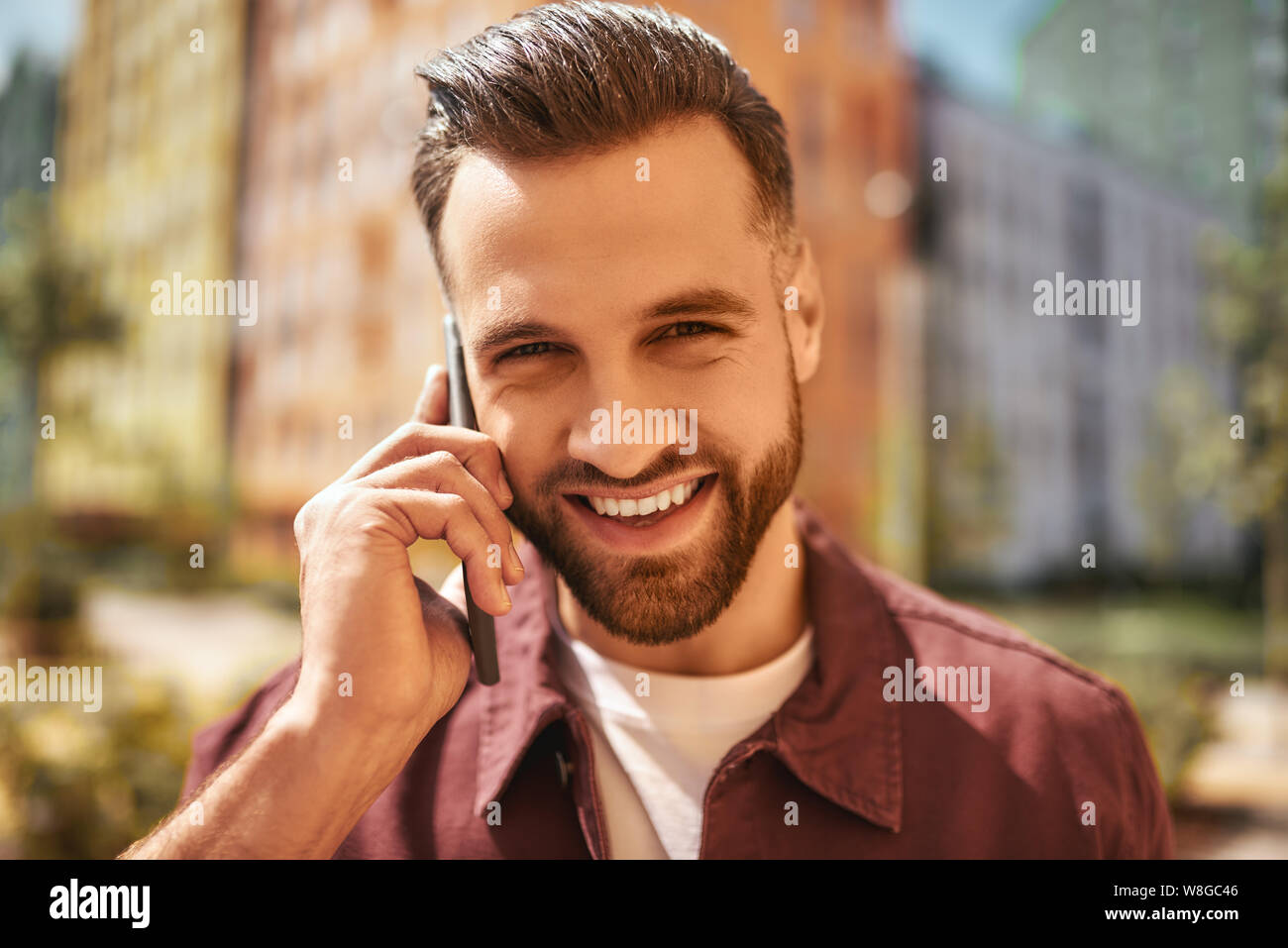 So gut, Sie zu hören Porträt von fröhlich und gut aussehend bärtigen Mann per Telefon reden und lächeln, während auf der Straße stehen. Gute Nachrichten. Digital. Kommunikation Stockfoto