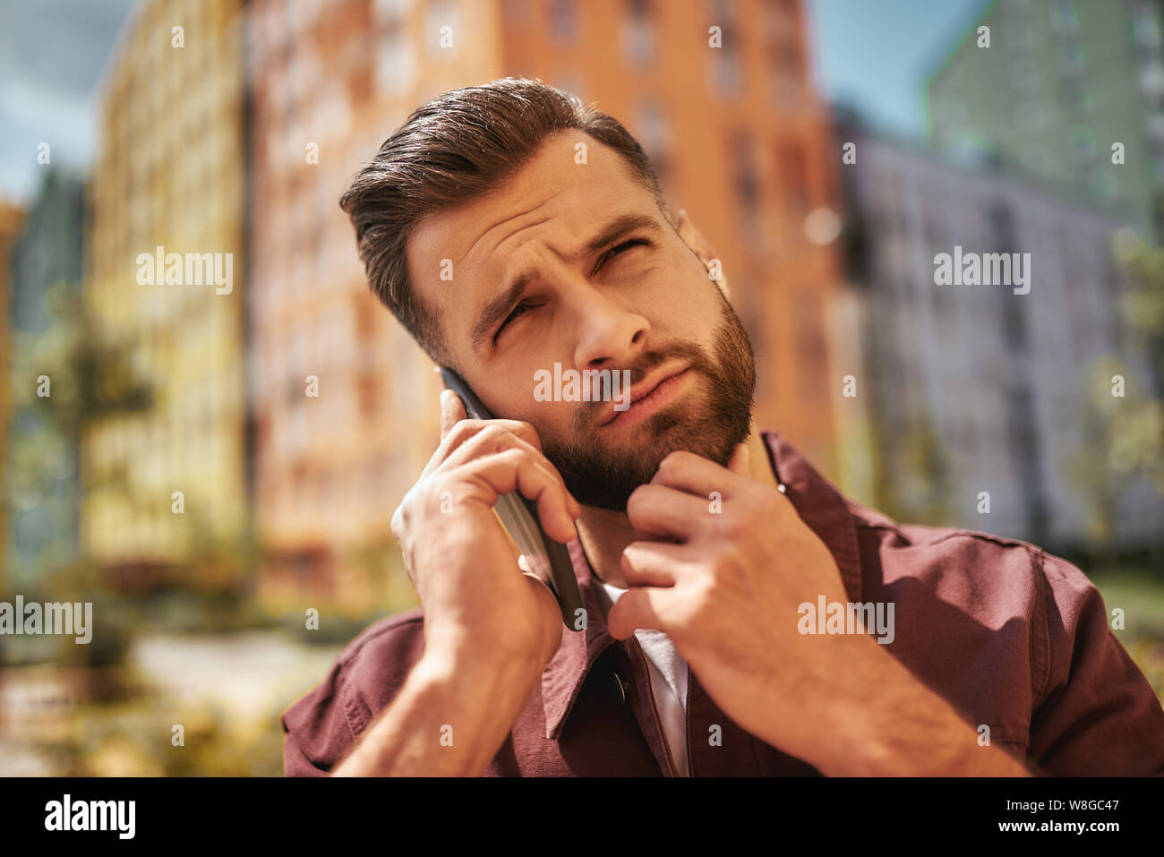 Hm... Portrait von nachdenklich bärtiger Mann sprechen über das Telefon und seine Stoppeln berühren beim Stehen auf der Straße. Schlechte Nachrichten. Digital. Kommunikation Stockfoto