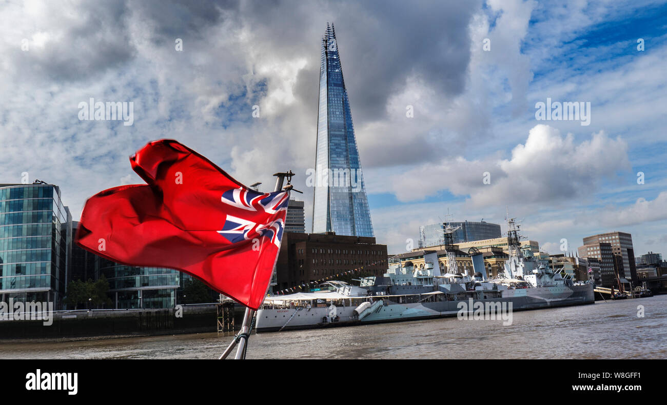 Die Londoner Shard und HMS Belfast mit Clipper River Boat Red Ensign Marine Flagge im Wind, mit dramatischen Himmel von Thames Clipper RB1 River Boat gesehen mit 'red Duster' Flagge. HMS Belfast, Der Shard und mehr London Place South Bank London SE1 UK Stockfoto
