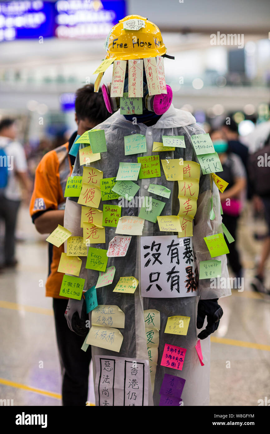 Eine Demonstrantin Handeln eine menschliche Lennon-mauer andere post-Meldungen auf seinem Körper während des Protestes am Flughafen zu lassen. Tausende Demonstranten in der Ankunftshalle des internationalen Flughafen Hong Kong unter der Bezeichnung "Grüße aus HKers Versammlung" die Aufmerksamkeit der internationale Reisende, die gerade in Hongkong über die aktuellen Unruhen in der Stadt gelandet zu fangen. Stockfoto