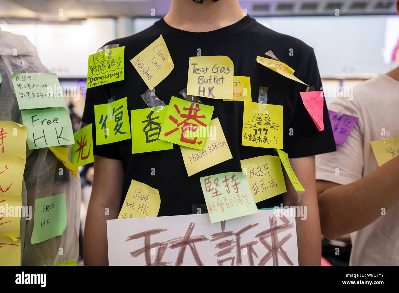 Eine Demonstrantin Handeln eine menschliche Lennon-mauer andere post-Meldungen auf seinem Körper während des Protestes am Flughafen zu lassen. Tausende Demonstranten in der Ankunftshalle des internationalen Flughafen Hong Kong unter der Bezeichnung "Grüße aus HKers Versammlung" die Aufmerksamkeit der internationale Reisende, die gerade in Hongkong über die aktuellen Unruhen in der Stadt gelandet zu fangen. Stockfoto