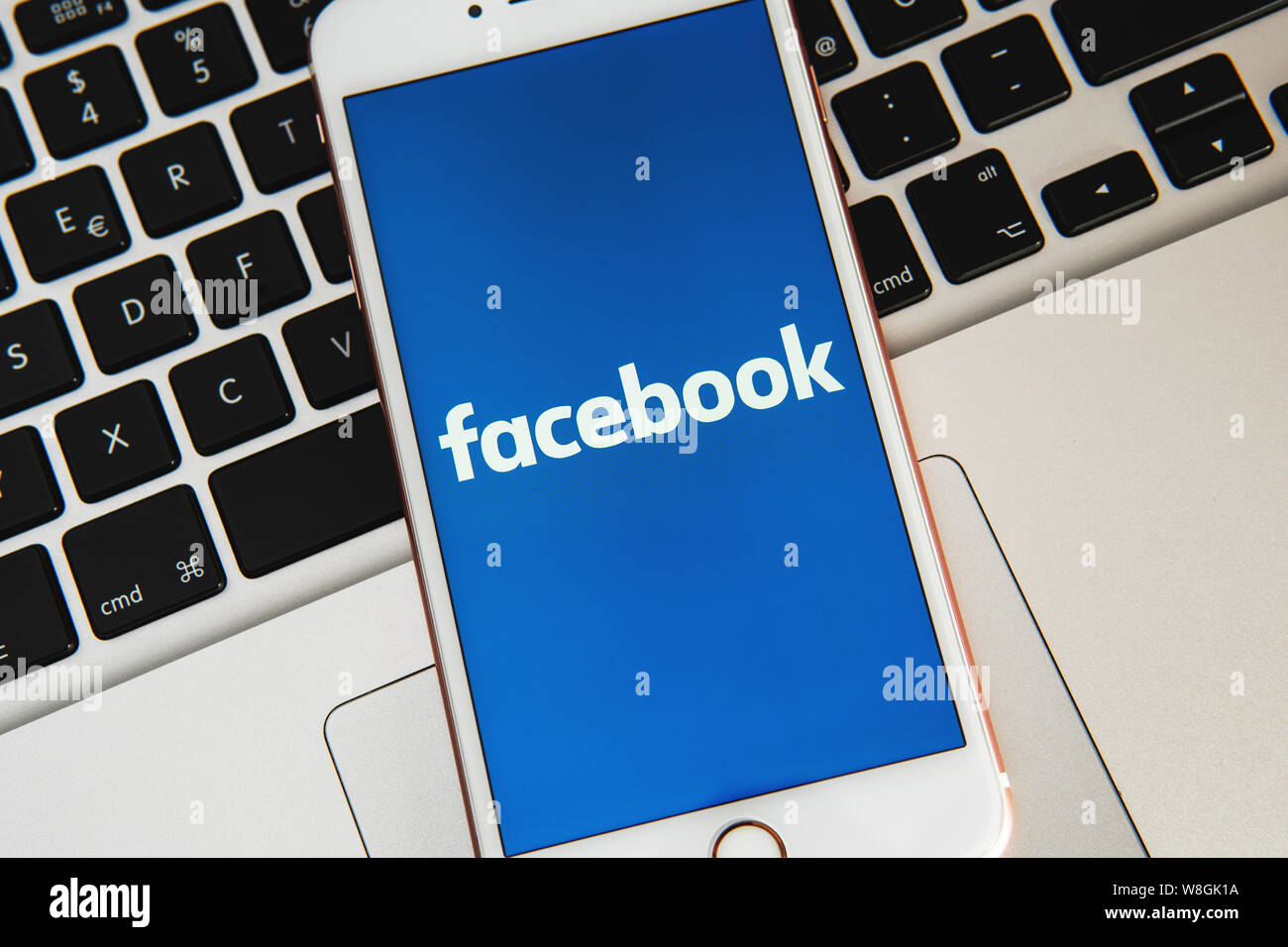 Weißes iPhone mit Logo der Social Media Facebook auf dem Bildschirm. Social media Symbol. Laptop Tastatur Hintergrund. Kann als Marketing Konzept verwendet werden. Stockfoto