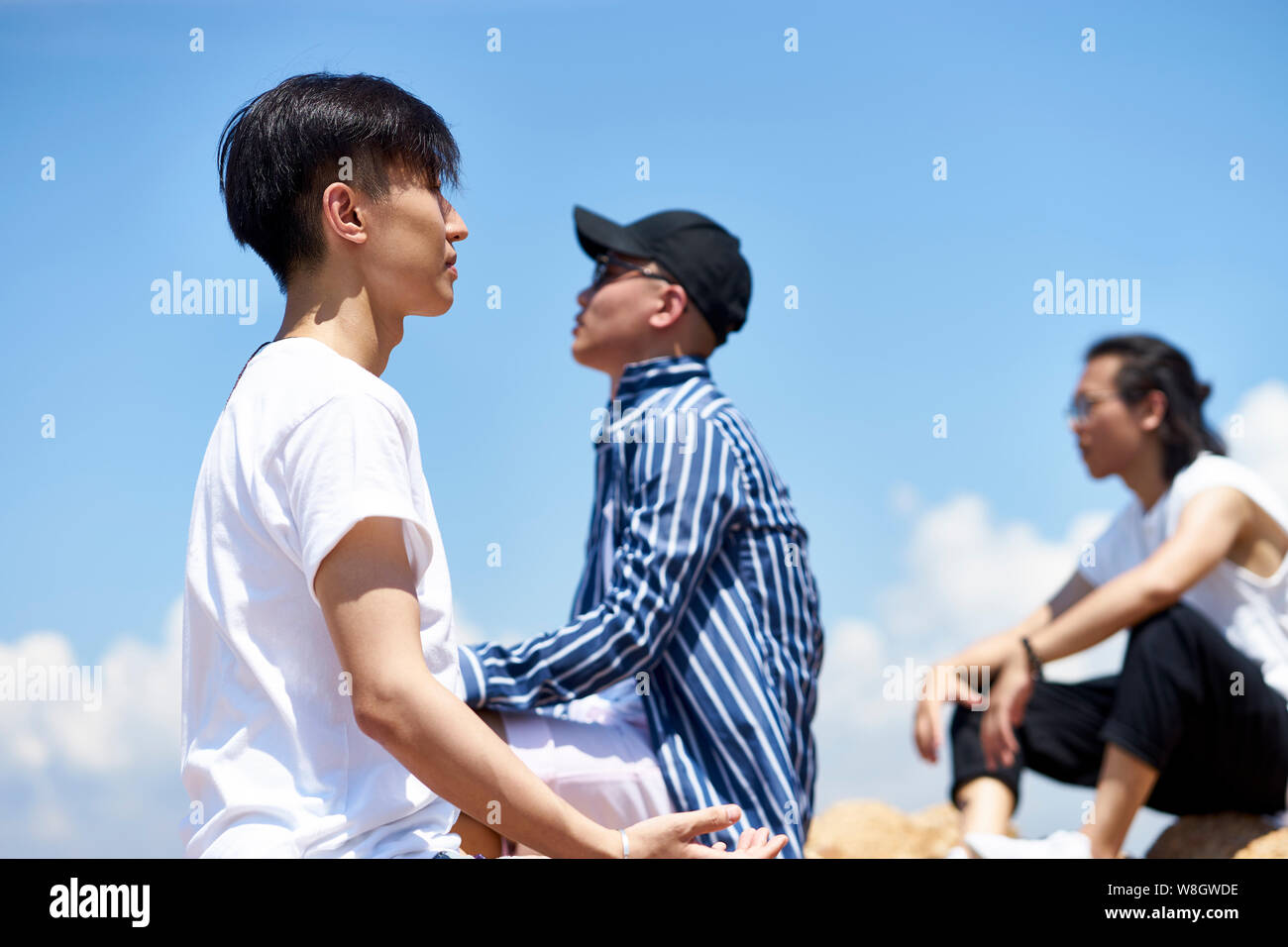 Gruppe von jungen asiatischen erwachsenen Männern saß oben auf der Felsen gegen den blauen Himmel Sonne und frische Luft genießen. Stockfoto