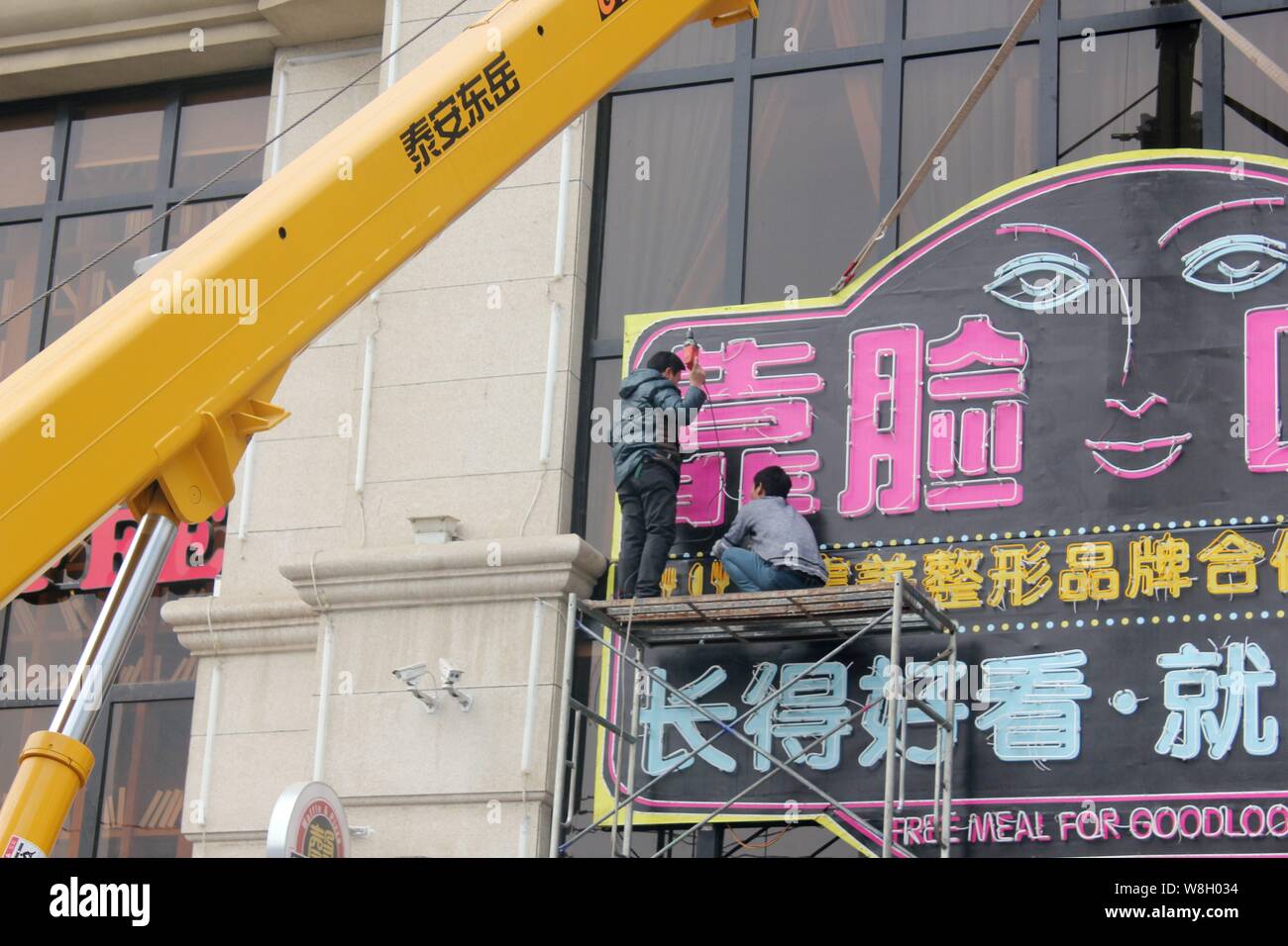 Chinesische Arbeiter unnail eine Anschlagtafel, bevor es mit dem Kran aus der Fassade des Restaurant bietet Speisen zu guten entfernt - suchen Kunden in Zh Stockfoto