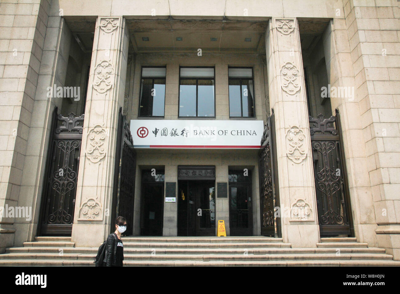 ---- Ein fussgänger tragen eine Maske an eine Filiale der Bank of China (BOC) in Shanghai, China, 1. Mai 2014. Bank von China feiert Stockfoto