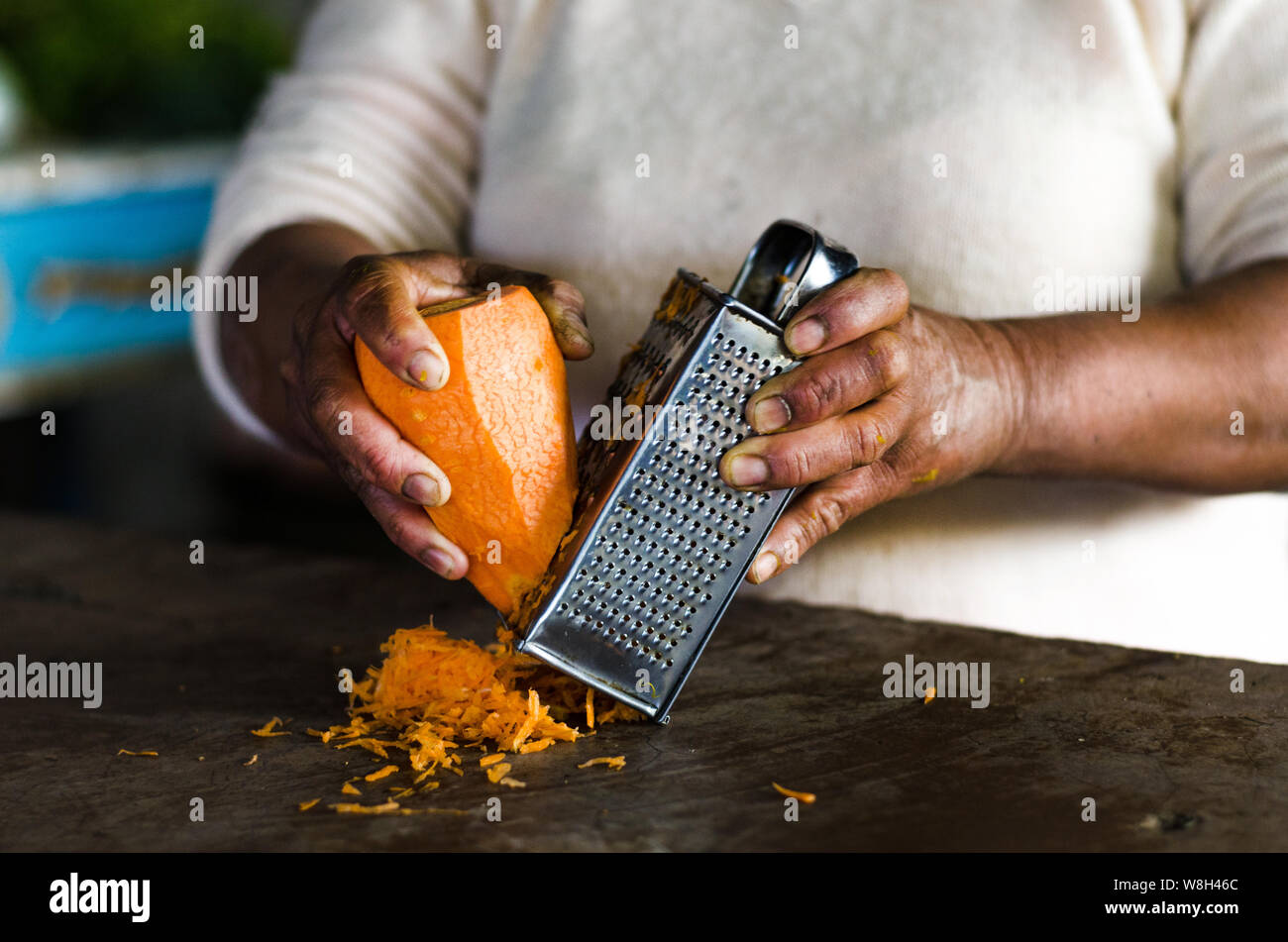 Hände einer Frau kratzen die Karotte, mit einem Metallreibebrett in der Hand Stockfoto