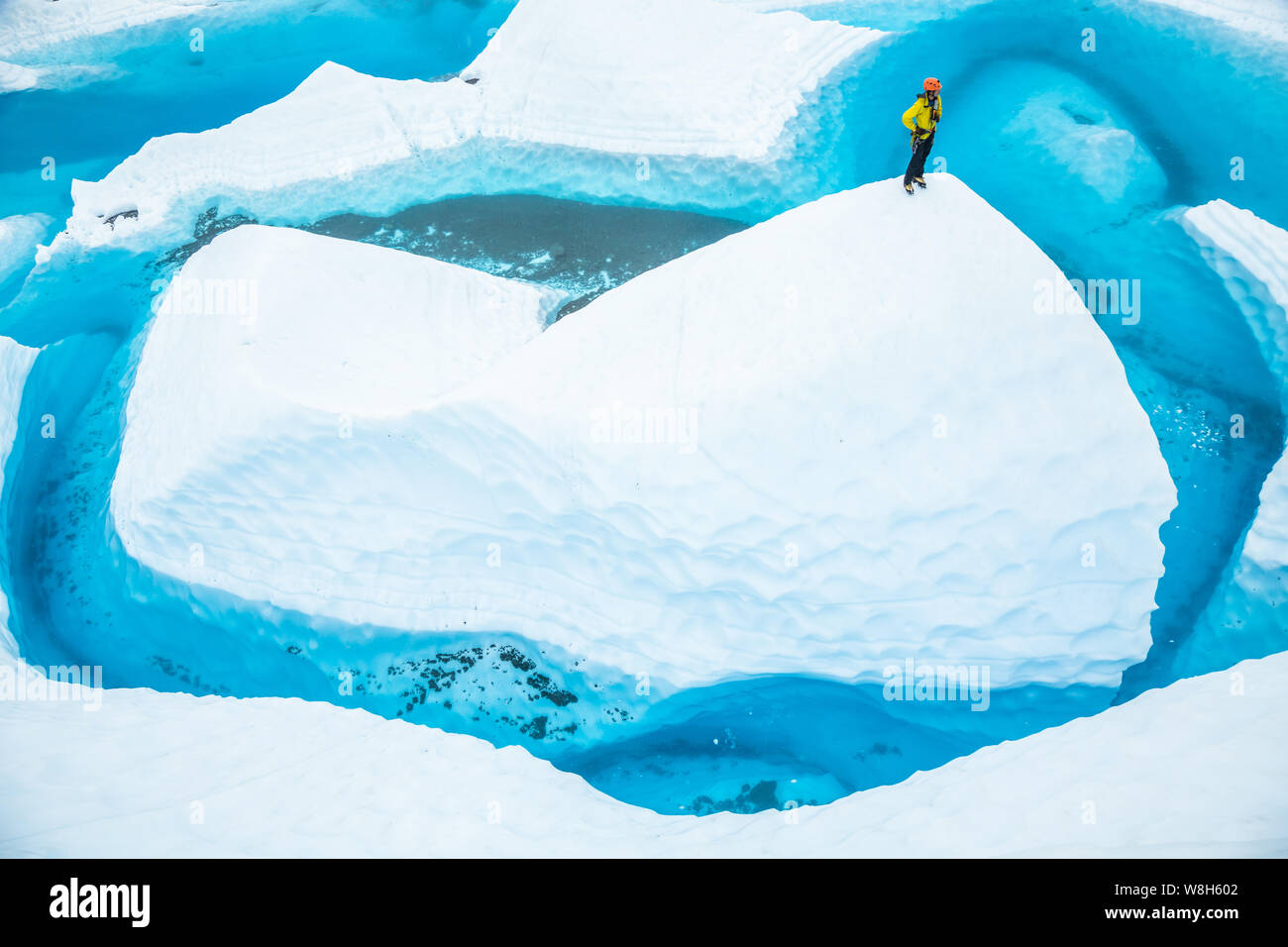 Nach dem Reiten in ein Kanu, ein junger Mann steht auf einem serac oder fin von Eis, das aus einem massiven blauen Pool. Der Supraglazialen See sitzt oben Stockfoto
