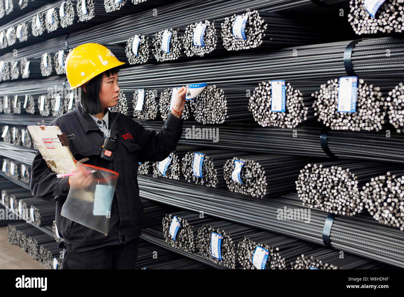 Ein weiblicher chinesischer Arbeiter prüft Stapel vom Verstärken von Stahl Stäbe im Lager eines Stahlwerks in Lanzhou Stadt, im Osten der chinesischen Provinz Jiangsu, Stockfoto
