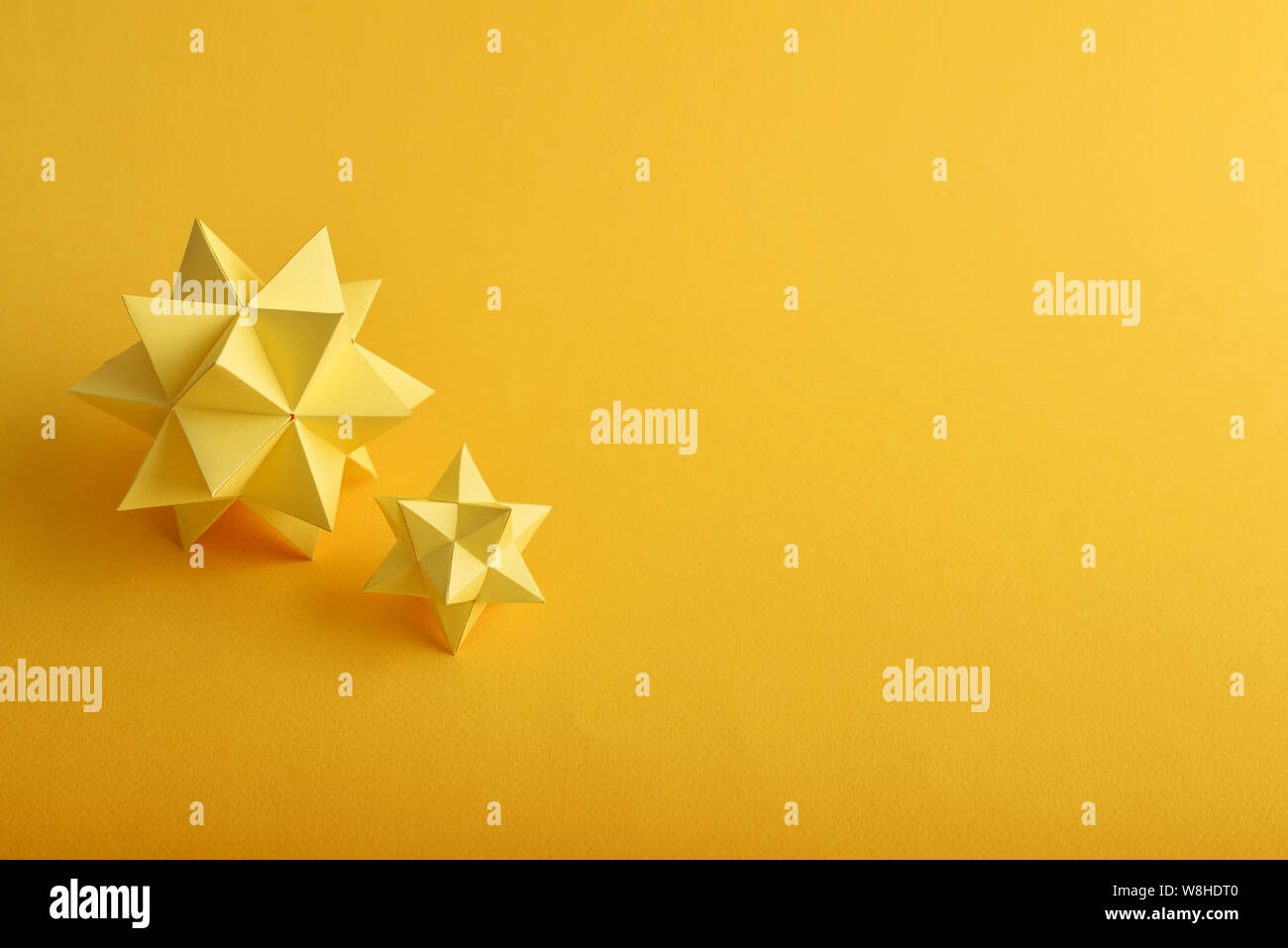 Zwei handgemachte gelbe Papier polyhedrons auf gelbem Hintergrund. Stockfoto