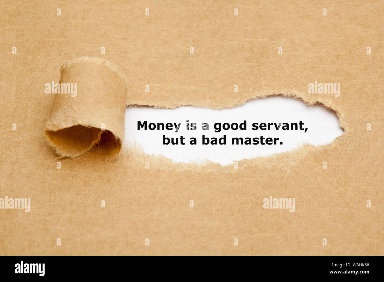 Das Zitat Geld ist ein guter Diener, aber ein schlechter Meister, hinter zerrissen braunes Papier erscheint. Stockfoto