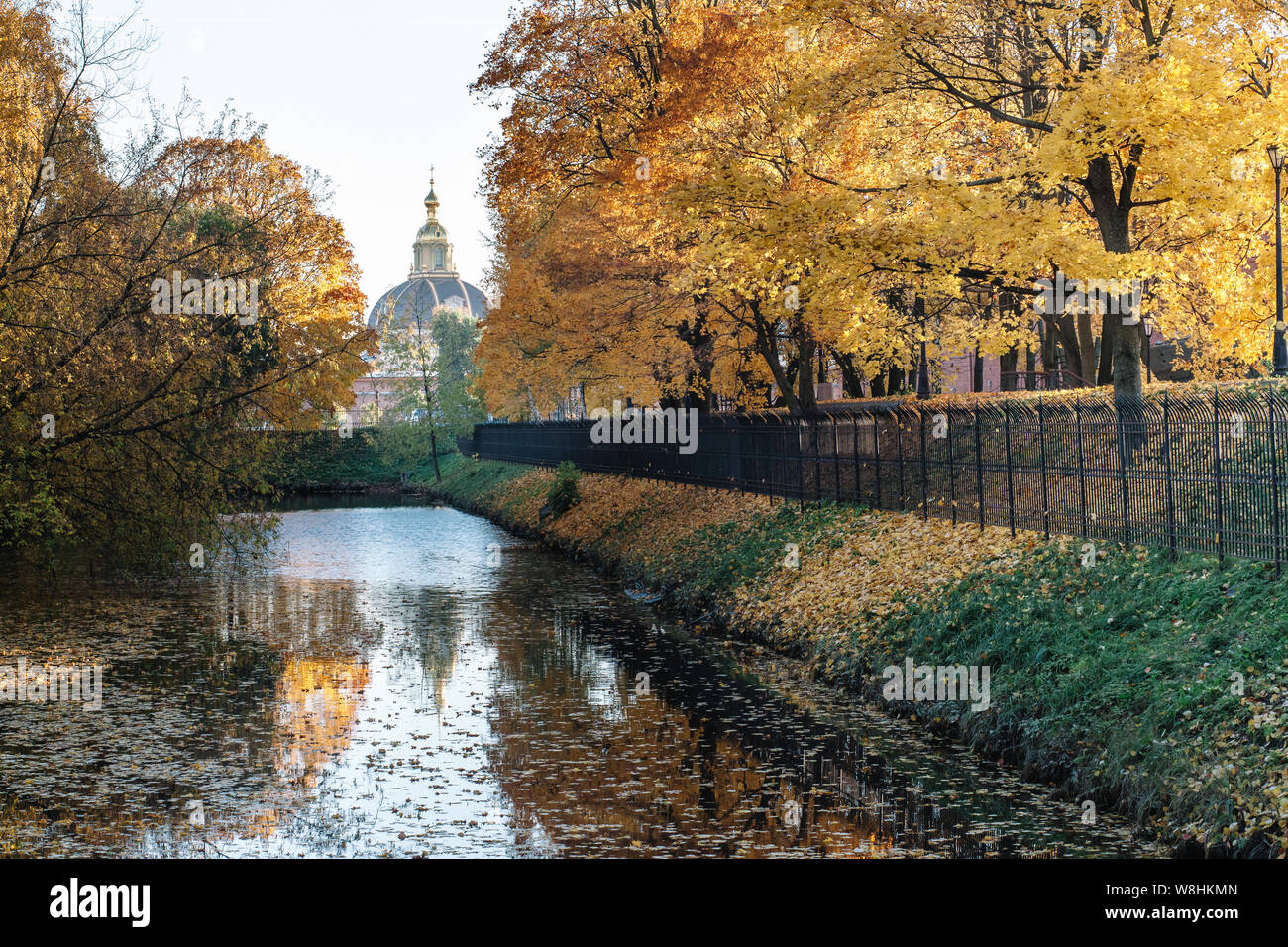 Schönen Herbst Landschaft mit gelben Bäume, Laub auf dem Wasser und einen Metallzaun. In der Ferne die Kuppel des Gebäudes. Stockfoto