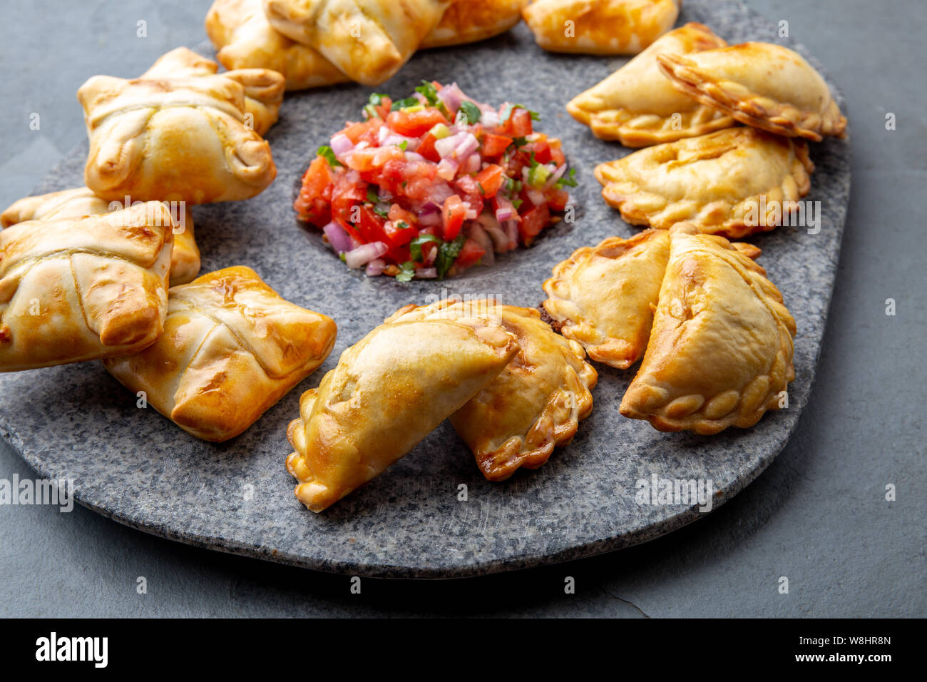 Verschiedene kleine Cocktail EMPANADAS auf der Steinplatte mit Tomatensauce und Guacamole. Grauer Hintergrund. Lateinamerikanische und Spanische typische Lebensmittel. Stockfoto