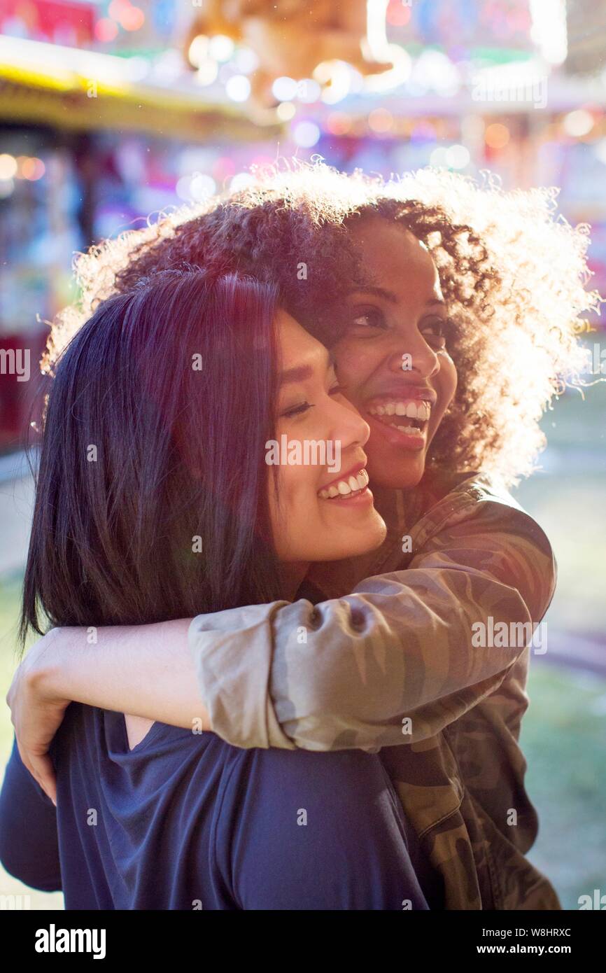 Zwei junge Frauen, die sich umarmen und Lachen im Sonnenlicht. Stockfoto