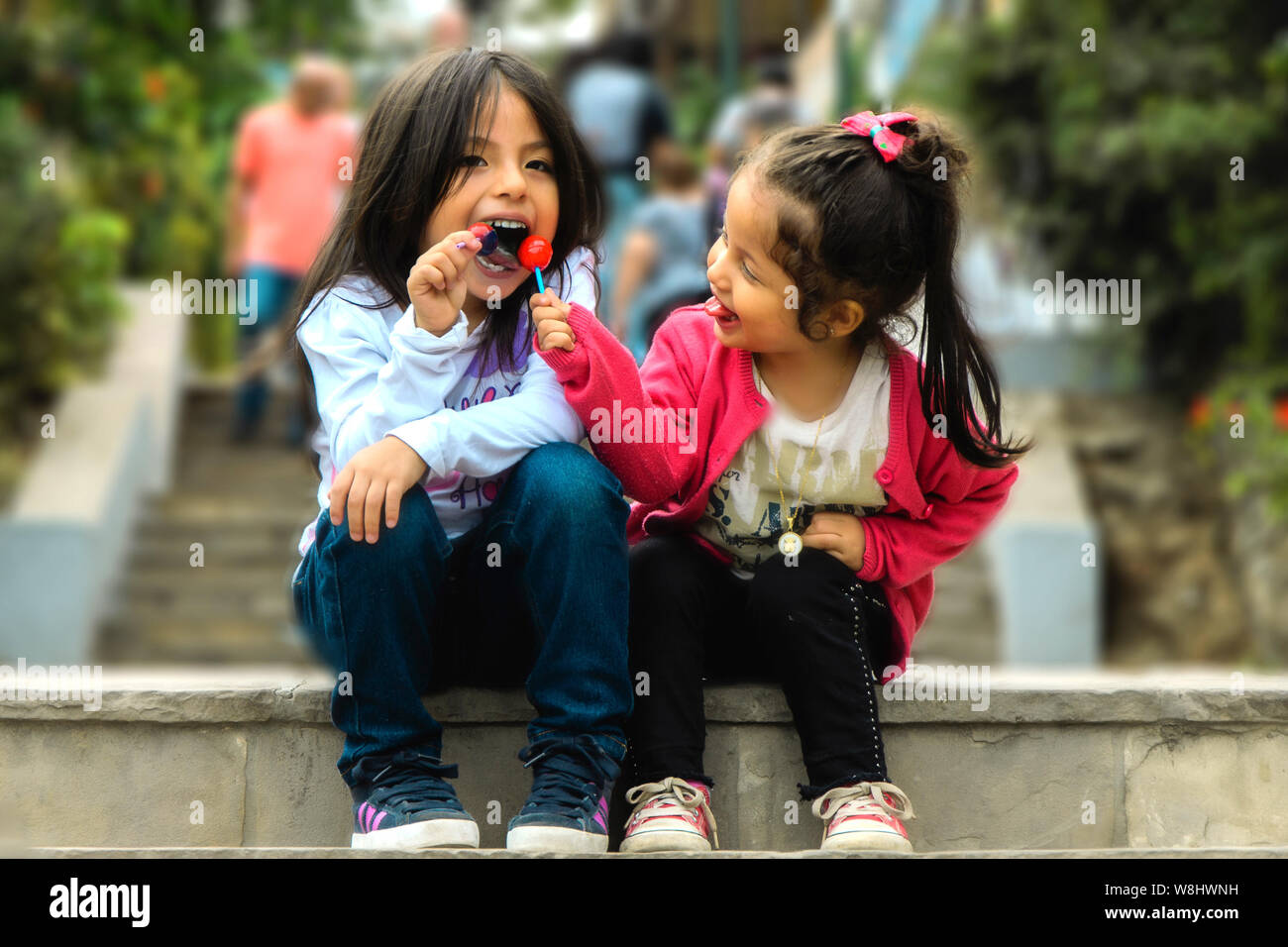 Zwei Mädchen sitzen und essen einen Lutscher im park, sommer Outdoor Portrait. beste Freunde Stockfoto