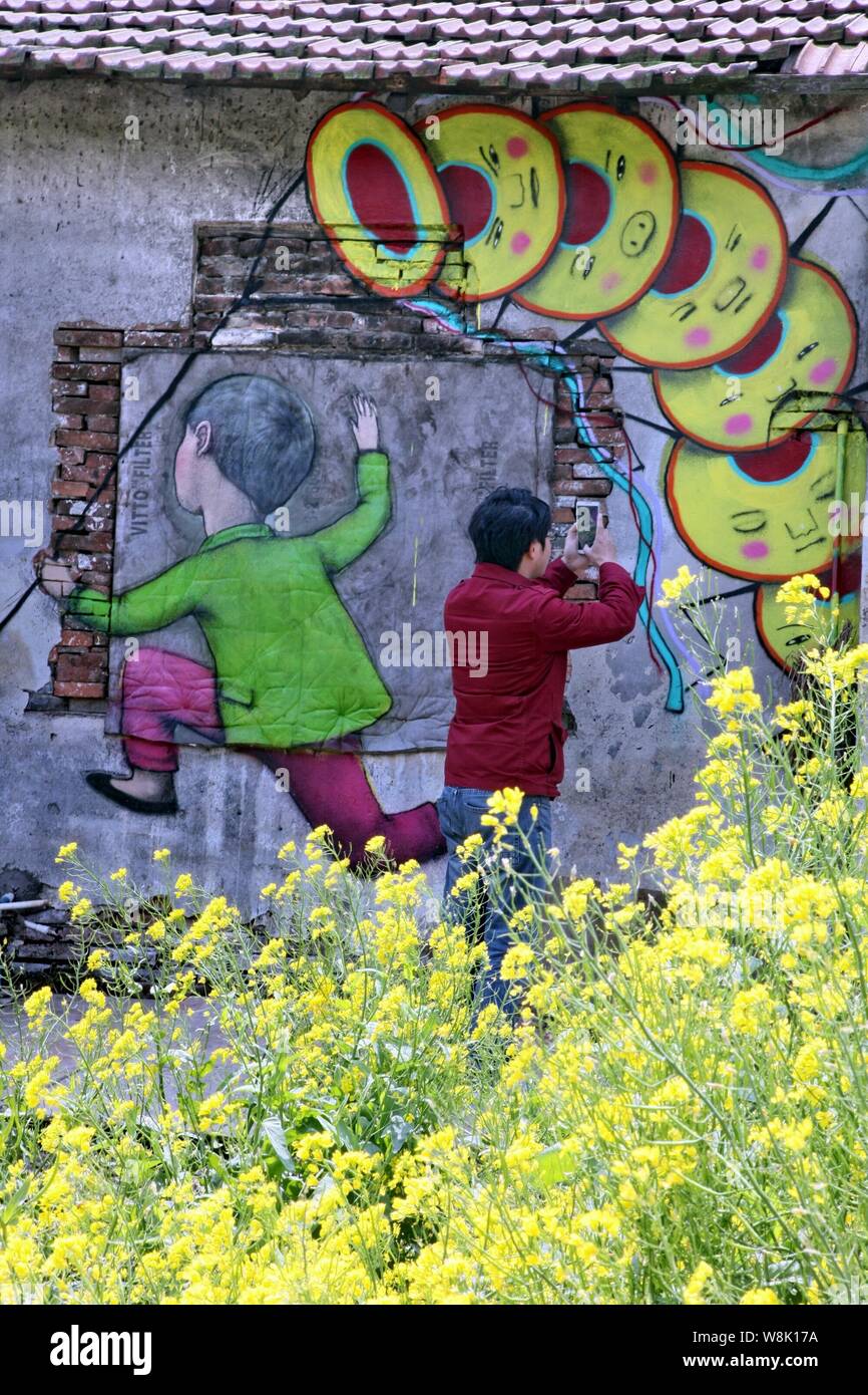 Ein Fußgänger nimmt Fotos auf einer Straße Kunst Malerei des französischen Künstlers Julien Seth Malland an der Wand eines Hauses in Xinyi Dorf Fengjing Stadt in Jins Stockfoto
