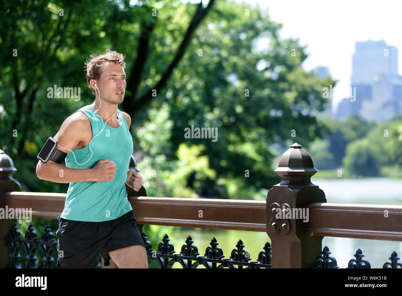 Man Joggen in der Stadt NEW YORK CITY mit Smartphone Armband. Männliche  Athlet runner läuft Musik Playlist auf Handy App- und Ohrhörer für Training  laufen im New Yorker Central Park im Sommer