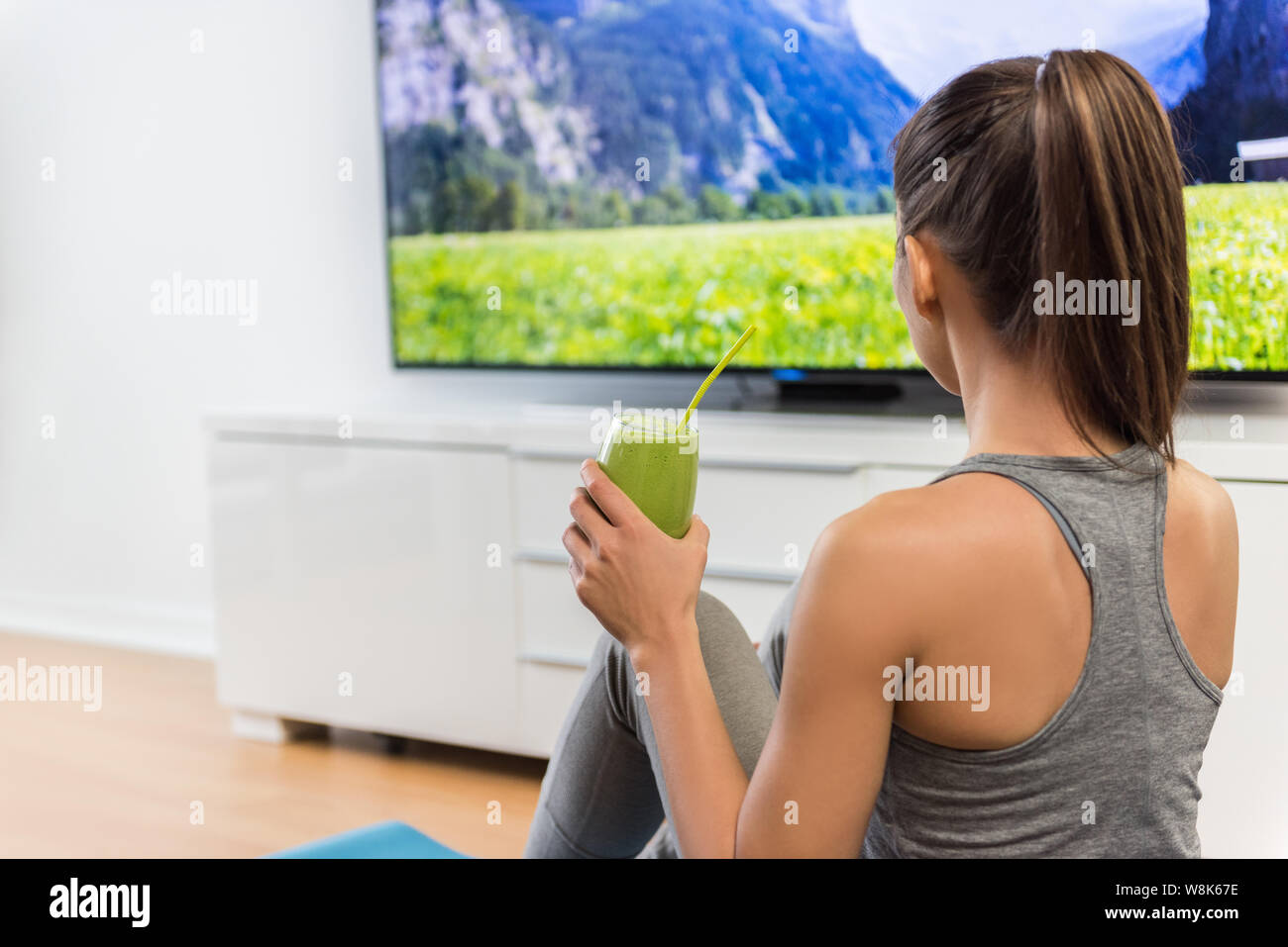 Home Frau trinkt grünen Smoothie watching tv-Show im Fernsehen mit Gewichtsverlust vegetarische Ernährung gesund Saft während der online Fitness dvd Workout videos im Wohnzimmer. Stockfoto