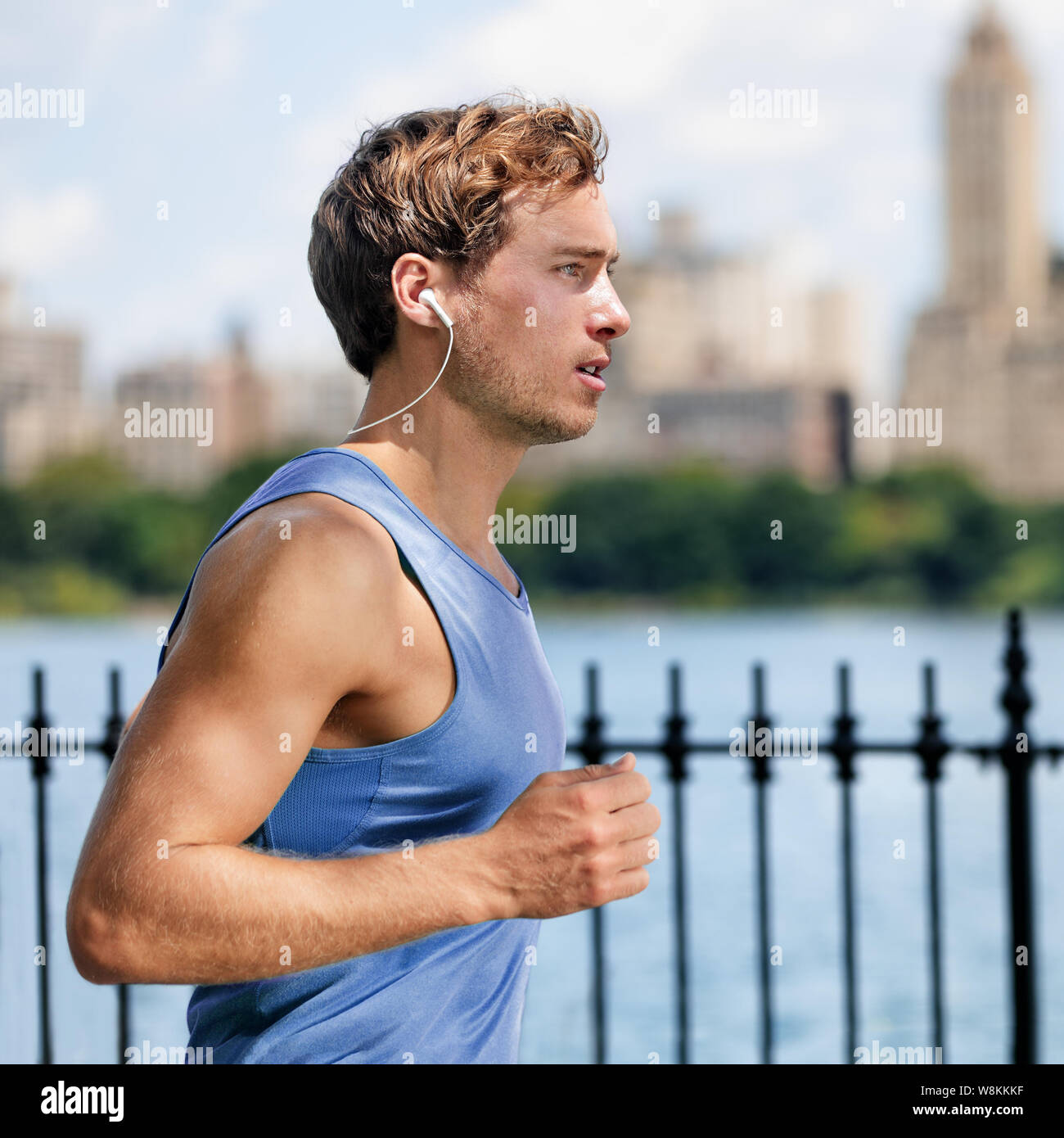 Der junge Mann im City Park, Abspielen von Musik mit drahtlosen Bluetooth In-Ear Kopfhörer Leben in einer gesunden, aktiven Lebensstil. Männliche Läufer oben Blau, cardio Training Training im Sommer. Stockfoto