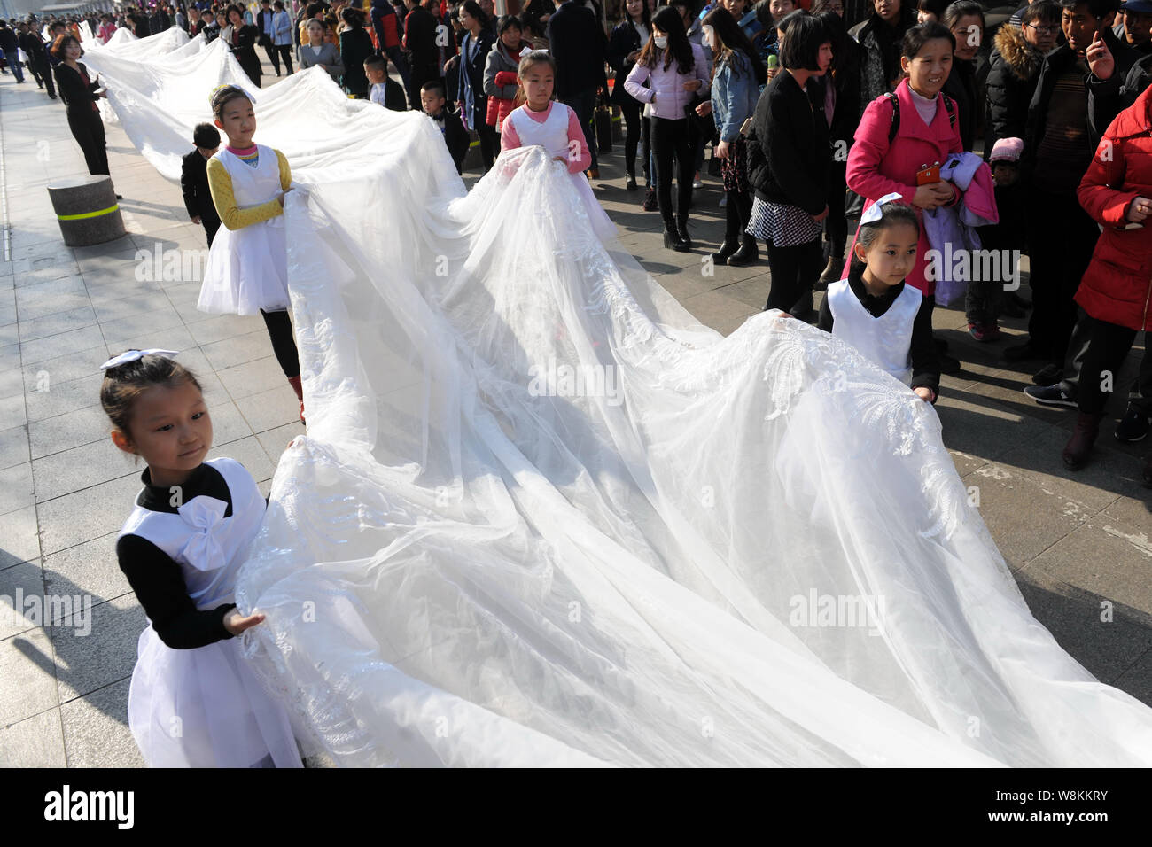 Junge Kinder und Mitarbeiterinnen und Mitarbeiter von einem Hochzeitskleid  Unternehmen tragen die 101 Meter lange Schwanz einer Brautkleid durch ein  Modell paradieren entlang einer Straße angezeigt Stockfotografie - Alamy