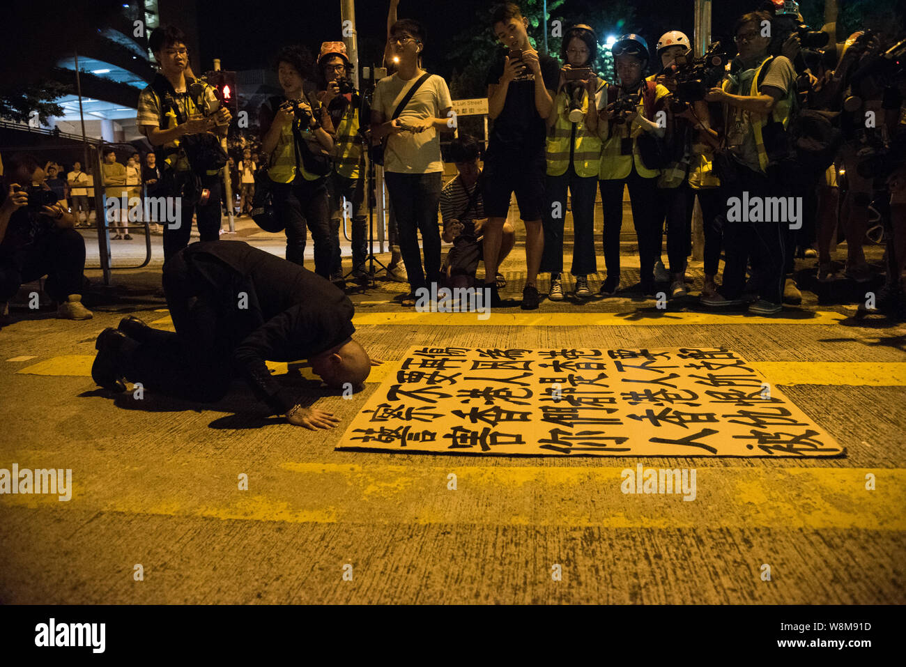 Eine Demonstrantin Verbeugungen vor der Bereitschaftspolizei mit seinem Zeichen. die Demonstranten auf den Straßen von Hongkong erneut, dieses Mal mit dem Hungry Ghost Festival als ein Weg, um gegen die Regierung zu demonstrieren. Die Demonstranten brennen verschiedenen Papier angeboten, die als eine Art Ahnen und Geister zu besänftigen. Stockfoto