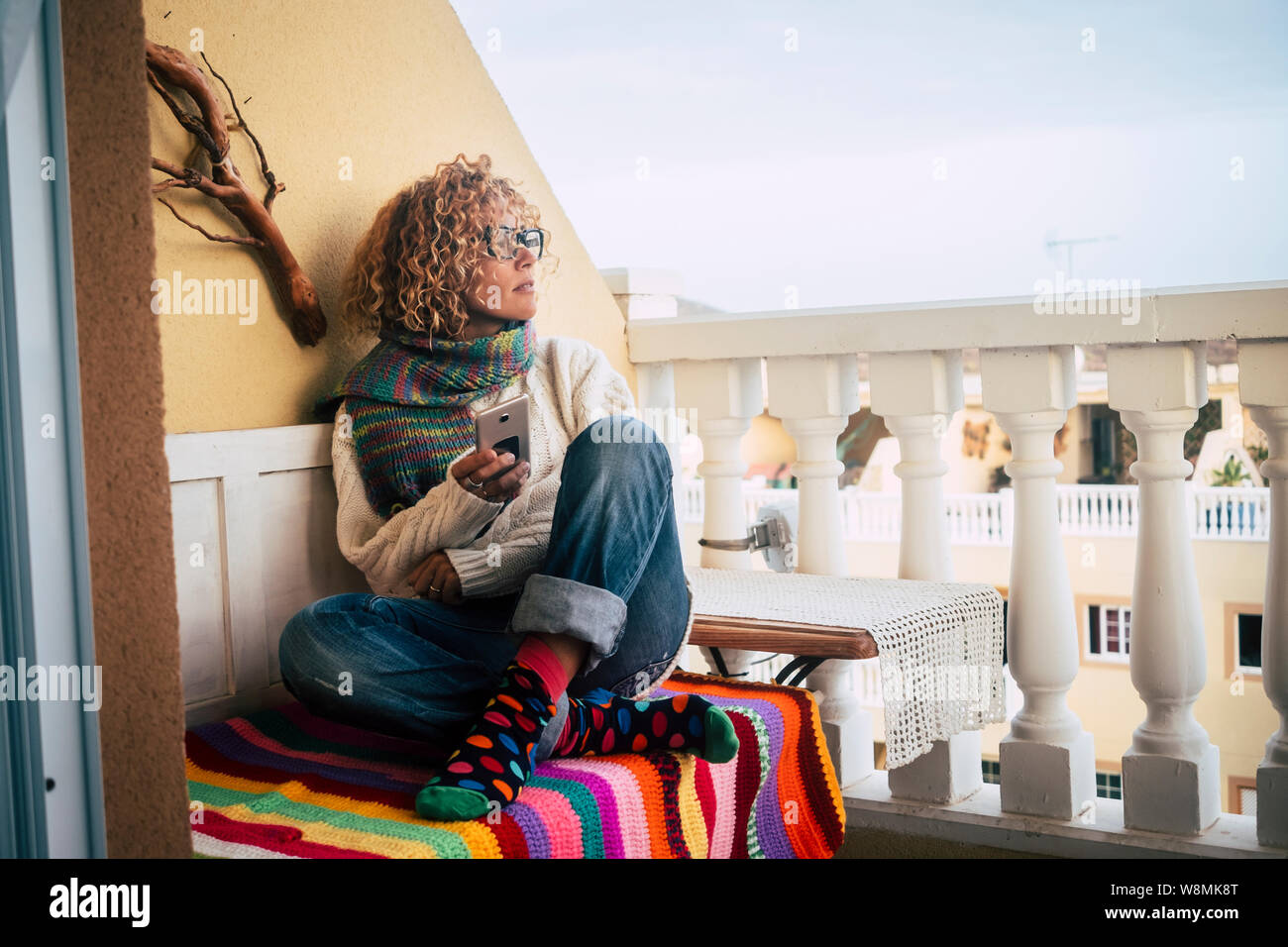 Nachdenklich kaukasischen Curly attraktive erwachsenen Frau mit Handy - Technologie Aktivität zu Hause auf der Terrasse für moderne Menschen in bunten Socken Stockfoto