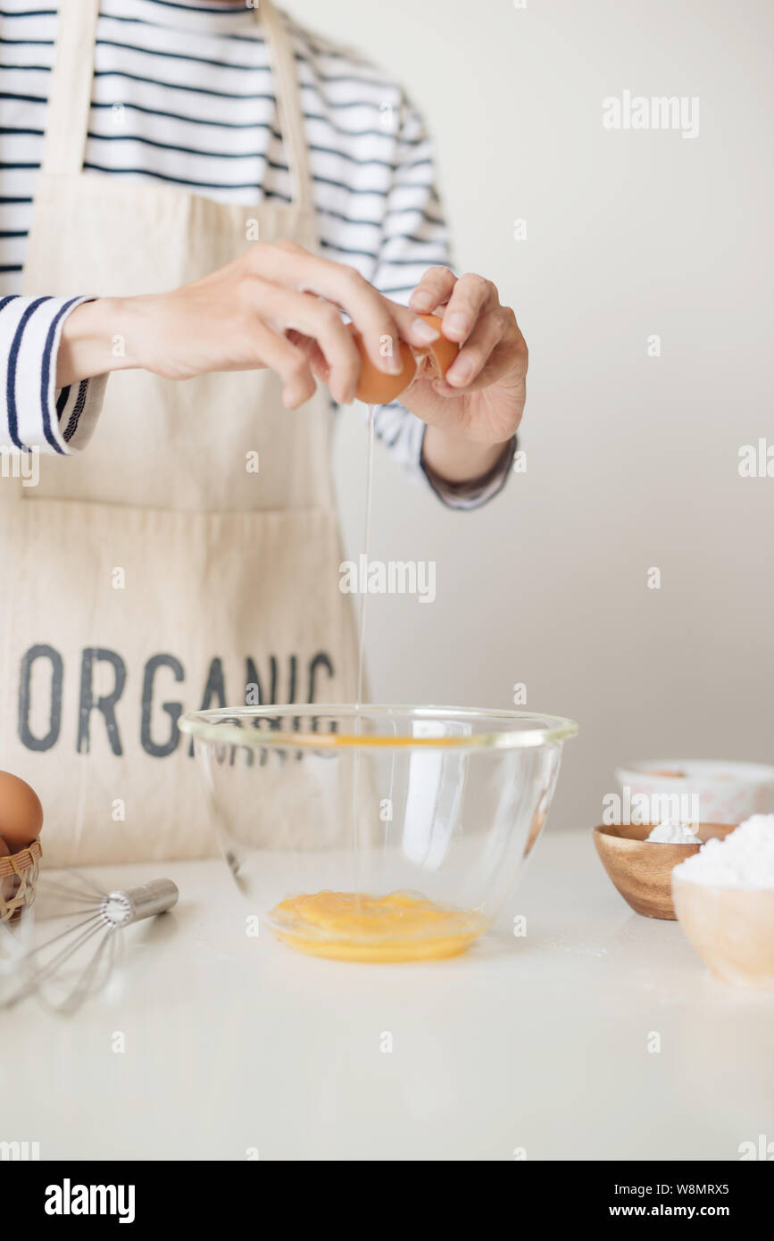 Horizontale schoss der schweren männlichen tragen beige Schürze brechen Ei in Metallschale Stockfoto