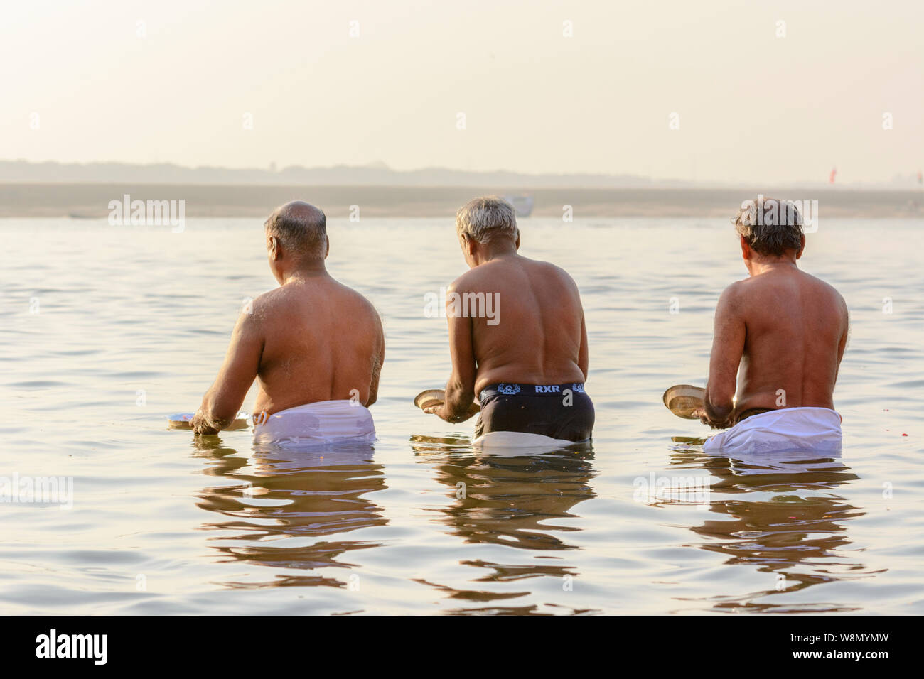 Drei indische Männer (Pilger) Gaben an die Götter (Hebe) im Fluss Ganges in Varanasi, Uttar Pradesh, Indien, Südasien. Stockfoto