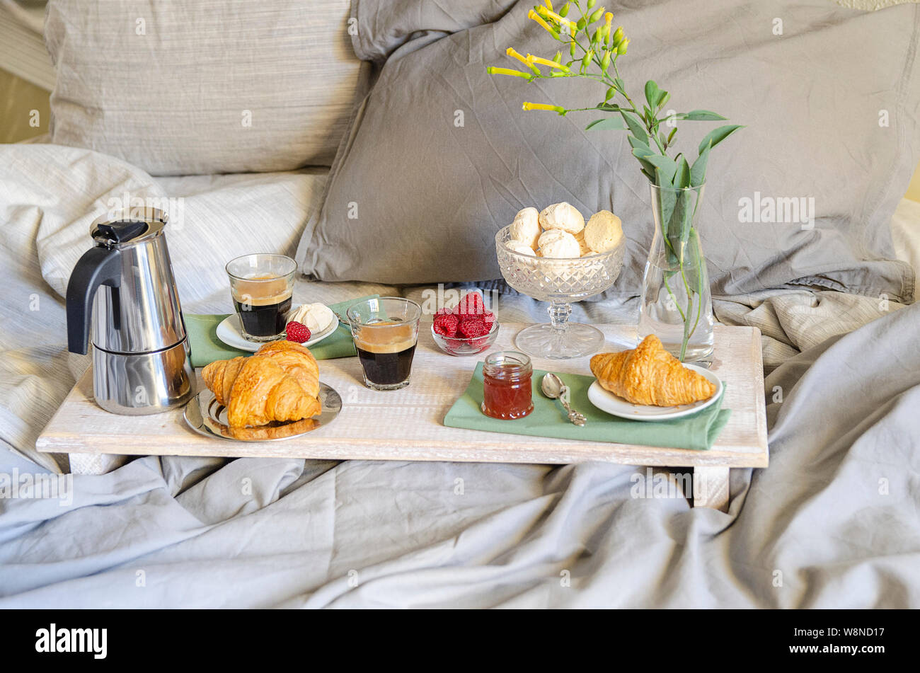 Romantisches Frühstück oder Brunch für zwei im Bett. Kaffeemaschine und  Kaffee Gläser, Croissants, Marmelade, Beeren, Baiser und Blumen auf Holz  fach Romantische Stockfotografie - Alamy