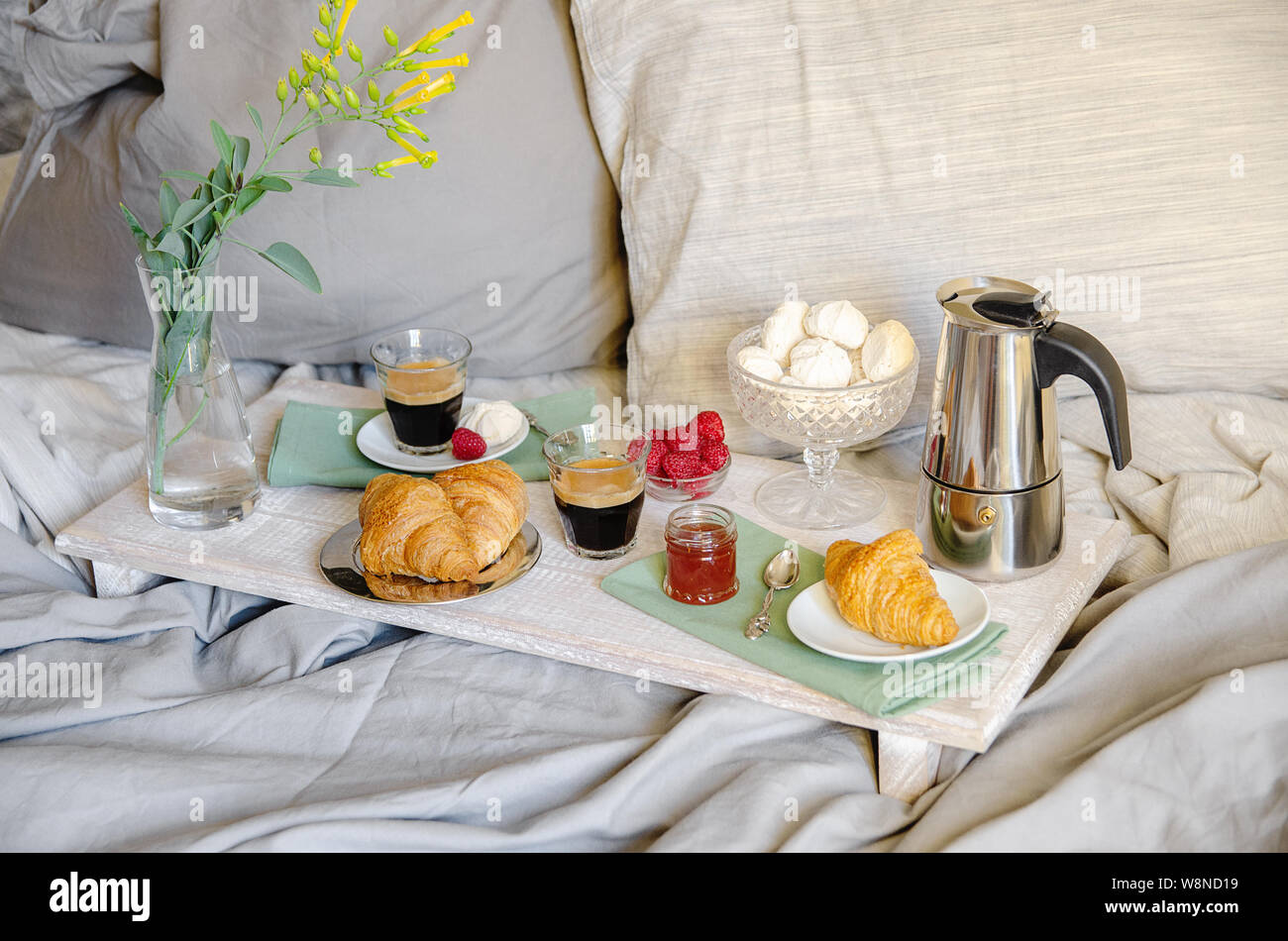 Romantisches Frühstück oder Brunch für zwei im Bett. Kaffeemaschine und  Kaffee Gläser, Croissants, Marmelade, Beeren, Baiser und Blumen auf Holz  fach Romantische Stockfotografie - Alamy