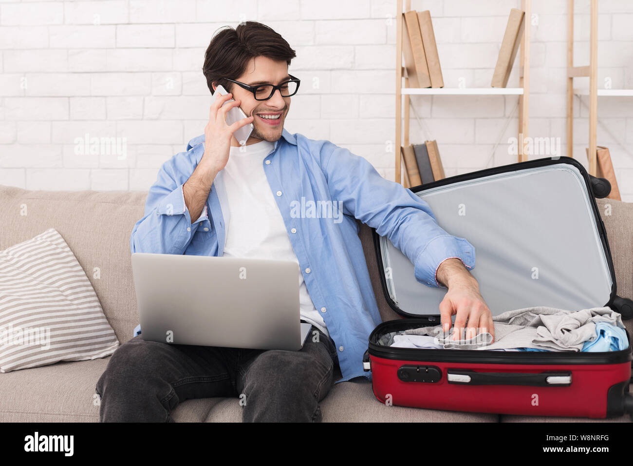 Junger Mann Vorbereitung für Reise und am Telefon sprechen Stockfoto
