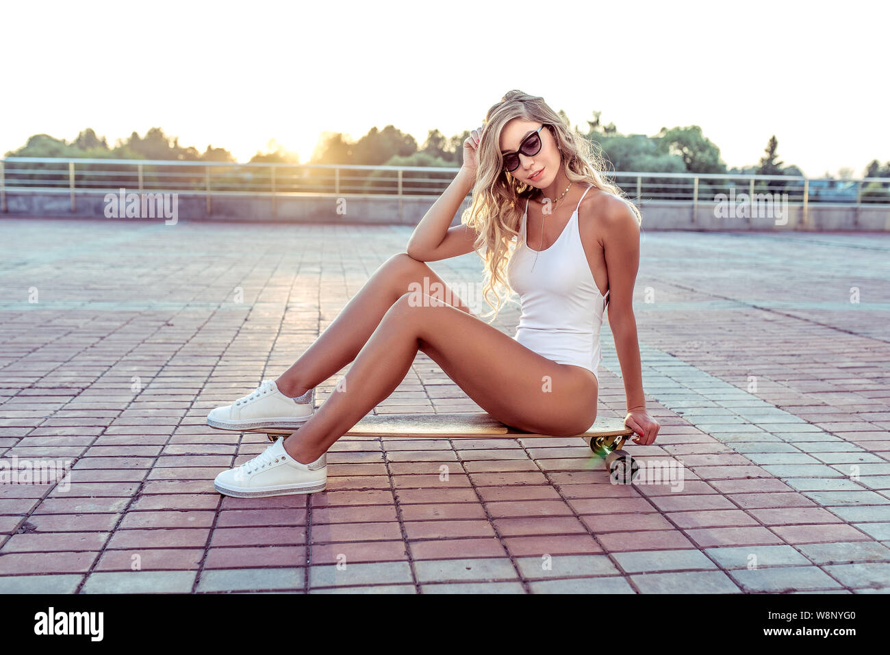 Mädchen im Sommer Stadt, sitzend Longboard Skateboard, lange Haare,  Sonnenbrille, Weiße Strampler Badeanzug Turnschuhe. Konzept modisch  stilvolle Frau Stockfotografie - Alamy