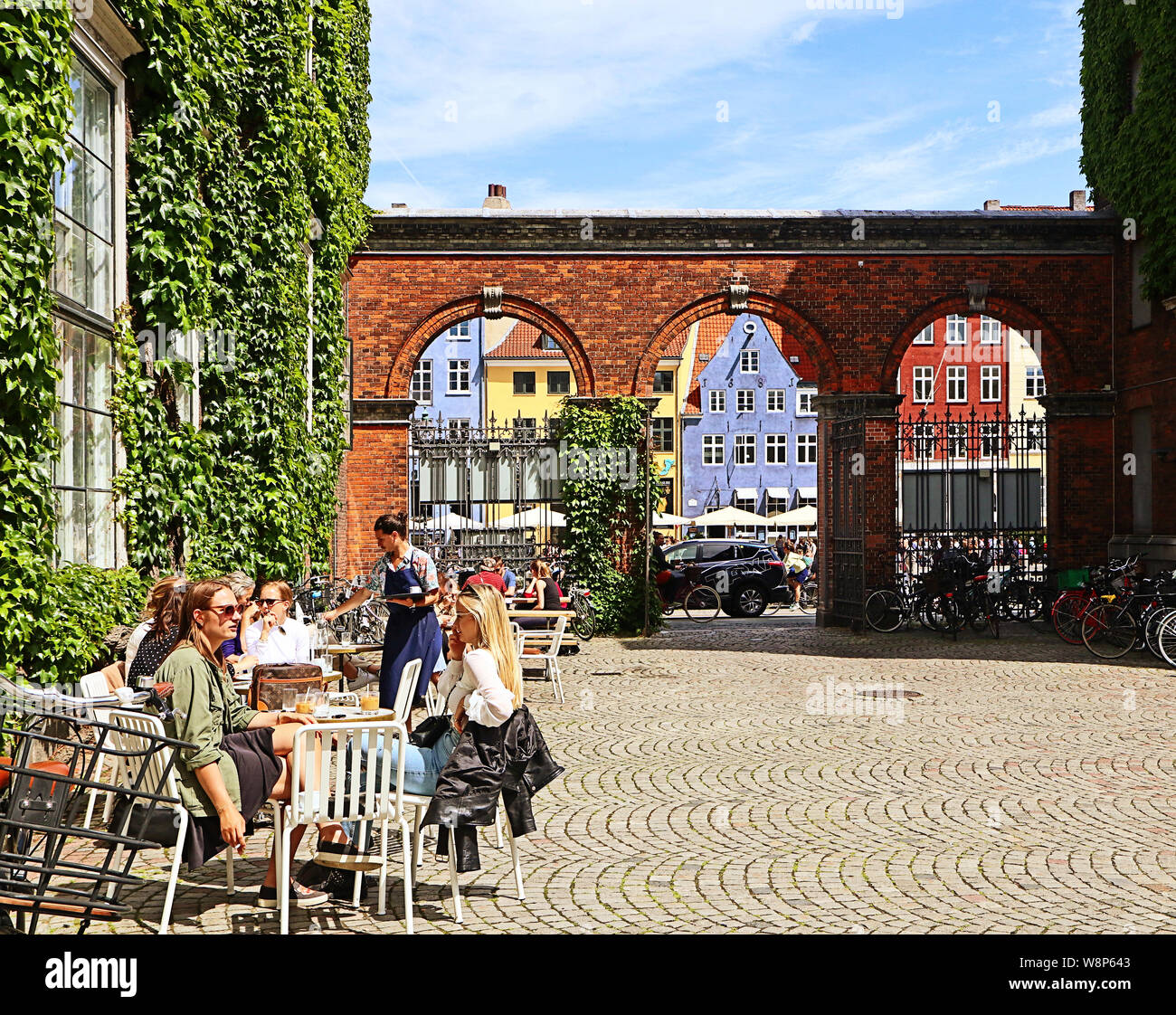 Kopenhagen, Dänemark - Juni 16, 2019 Leute in der Sonne an der Cafeteria im Hof des Schloss Charlottenborg entspannen Sie sich mit der Auffassung von Nyhavn Stockfoto
