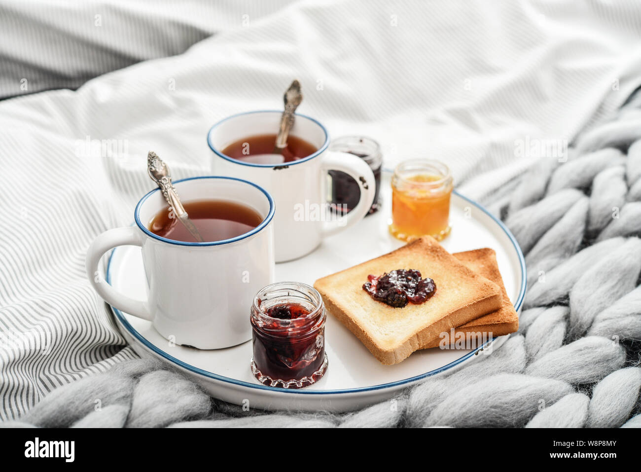 Fach mit zwei Tassen schwarzen Tee, verschiedene Marmelade in Gläser und Toast zum Frühstück am Bett closeup Stockfoto