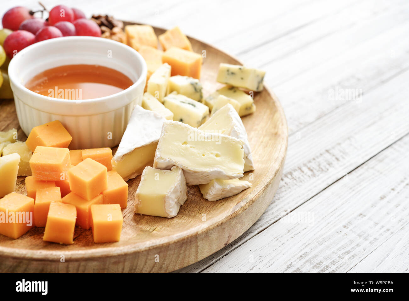 Käseplatte - verschiedene Arten von Käse mit Honig, Nüsse und Trauben auf einem weißen Holz- Hintergrund: Detailansicht Stockfoto