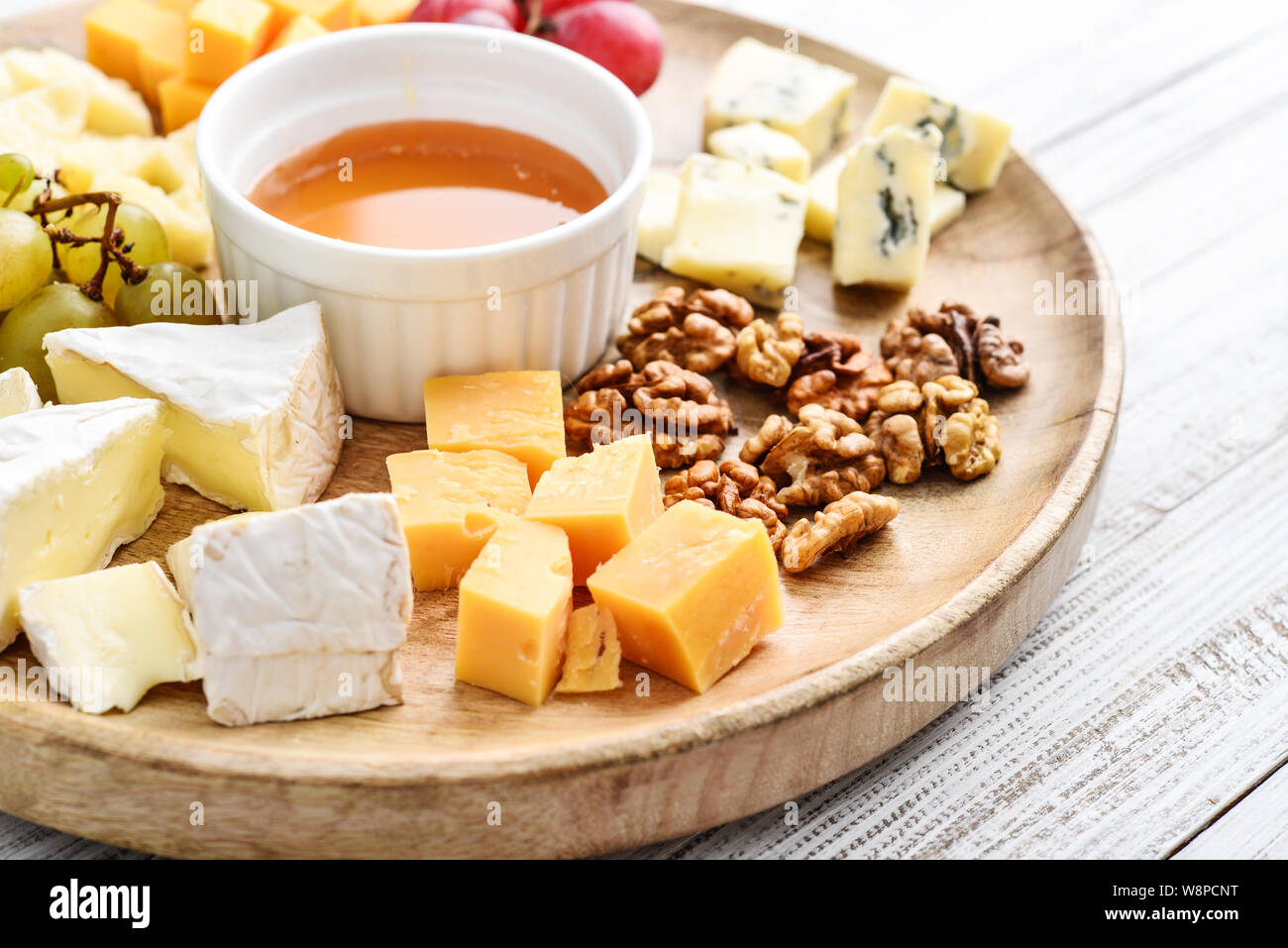 Käseplatte - verschiedene Arten von Käse mit Honig, Nüsse und Trauben auf einem weißen Holz- Hintergrund closeup Stockfoto