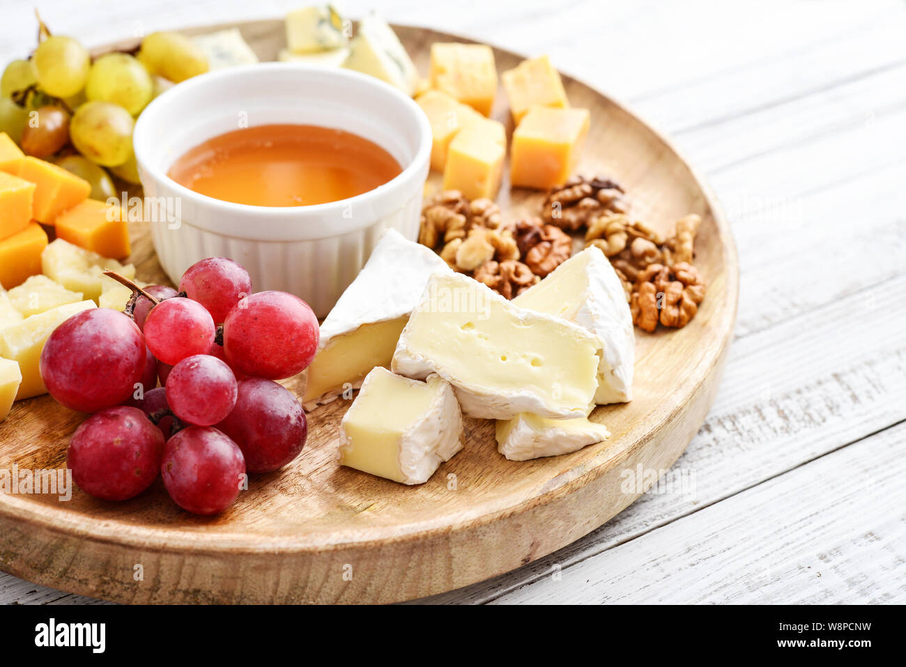 Käseplatte - verschiedene Arten von Käse mit Honig, Nüsse und Trauben auf einem weißen Holz- Hintergrund closeup Stockfoto