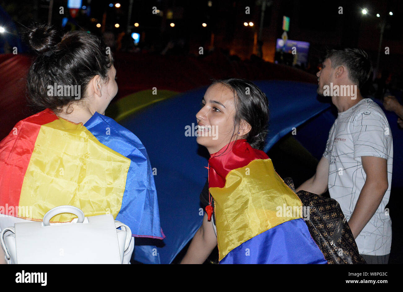 Bukarest, Rumänien - 10. AUGUST 2019: Rund 20.000 Menschen protestieren in Piata Victoriei am Jahrestag der Gendarmen Angriff auf Demonstranten. Schütteln eine große rumänische Flagge. Stockfoto