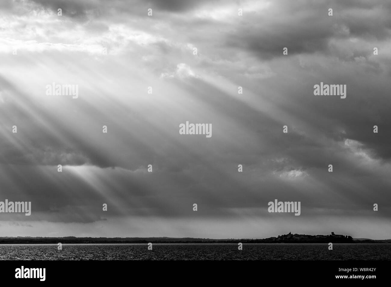 Sonnenstrahlen mit dunklen Wolken im Hintergrund und den Trasimenischen See (Umbrien, Italien) unter Stockfoto