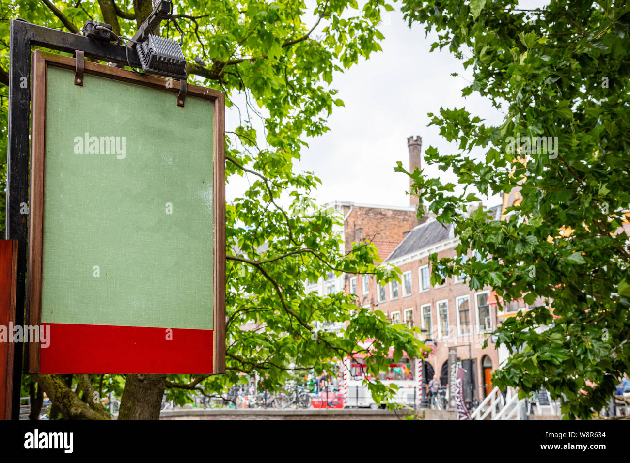 Grüne Brett leer mit Holzrahmen im Freien, blur Gebäude und Bäume Hintergrund. Utrecht, Niederlande, historisches Zentrum. Werbung mockup Vorlage Stockfoto