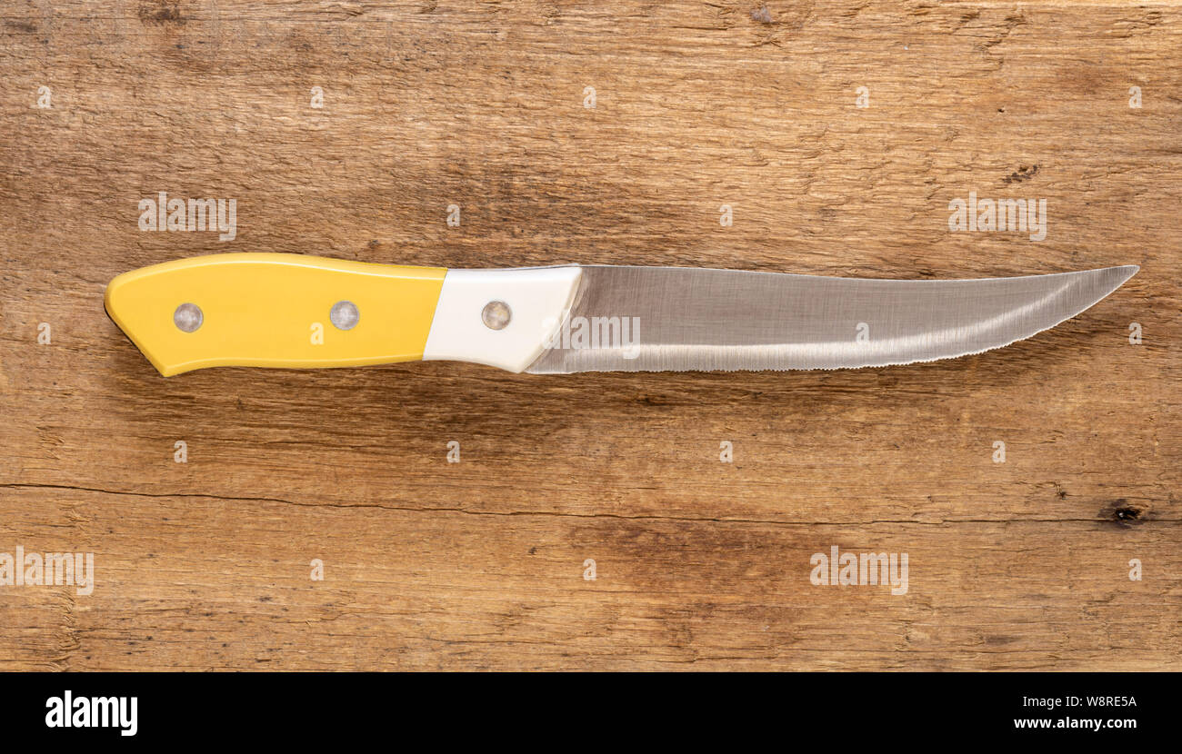 Küchenmesser, mit gelbem und weißem Griff und Stahl Sägezahn auf einem natürlichen Holz Hintergrund Blade. Stockfoto