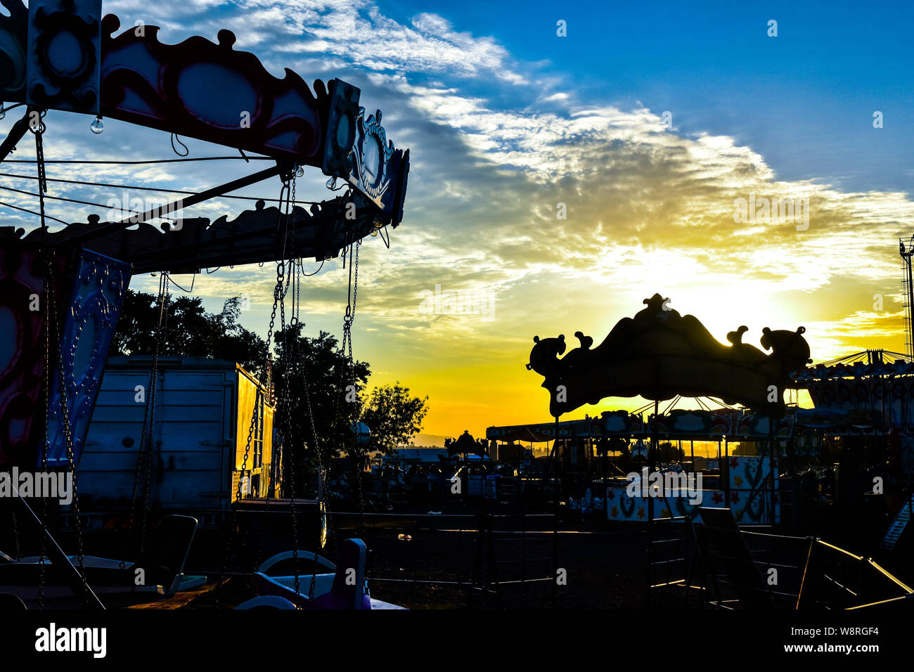 Am frühen Morgen goldenen Glühen am Jahrmarkt mit großer Silhouette, dramatischer Himmel und eine Auswahl von Fahrten in den Horizont Stockfoto