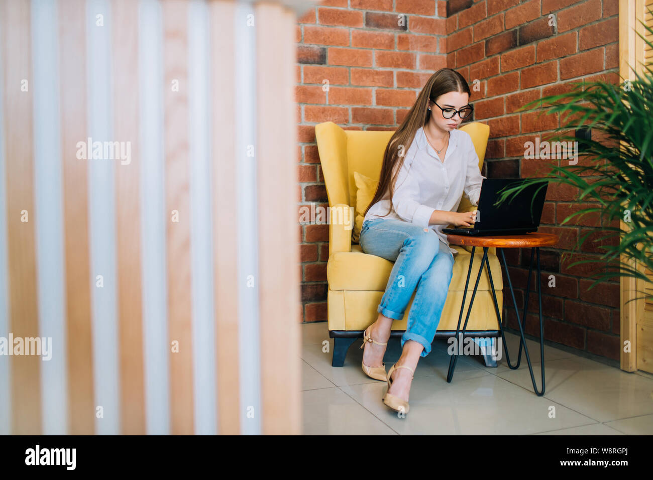 Junge erfolgreiche Geschäftsfrau in Gläsern auf einem schwarzen Laptop in einem Coffee Shop. Stockfoto