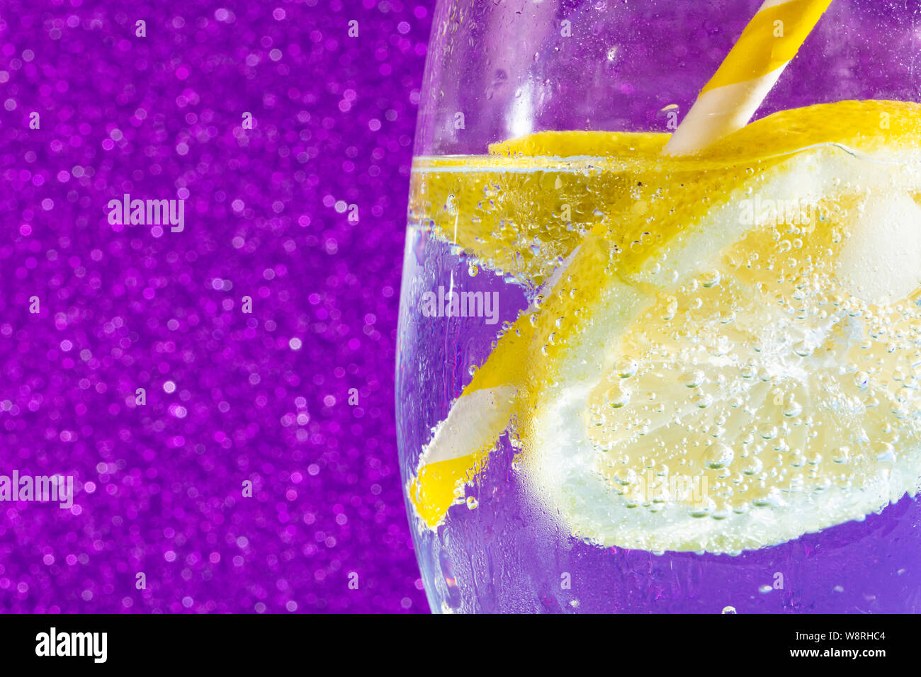 Frisch Soda mit Blasen einen Eiswürfel, einer Scheibe Zitrone und ein Stroh auf eine glänzende lila Hintergrund. Freier Platz für Text Stockfoto