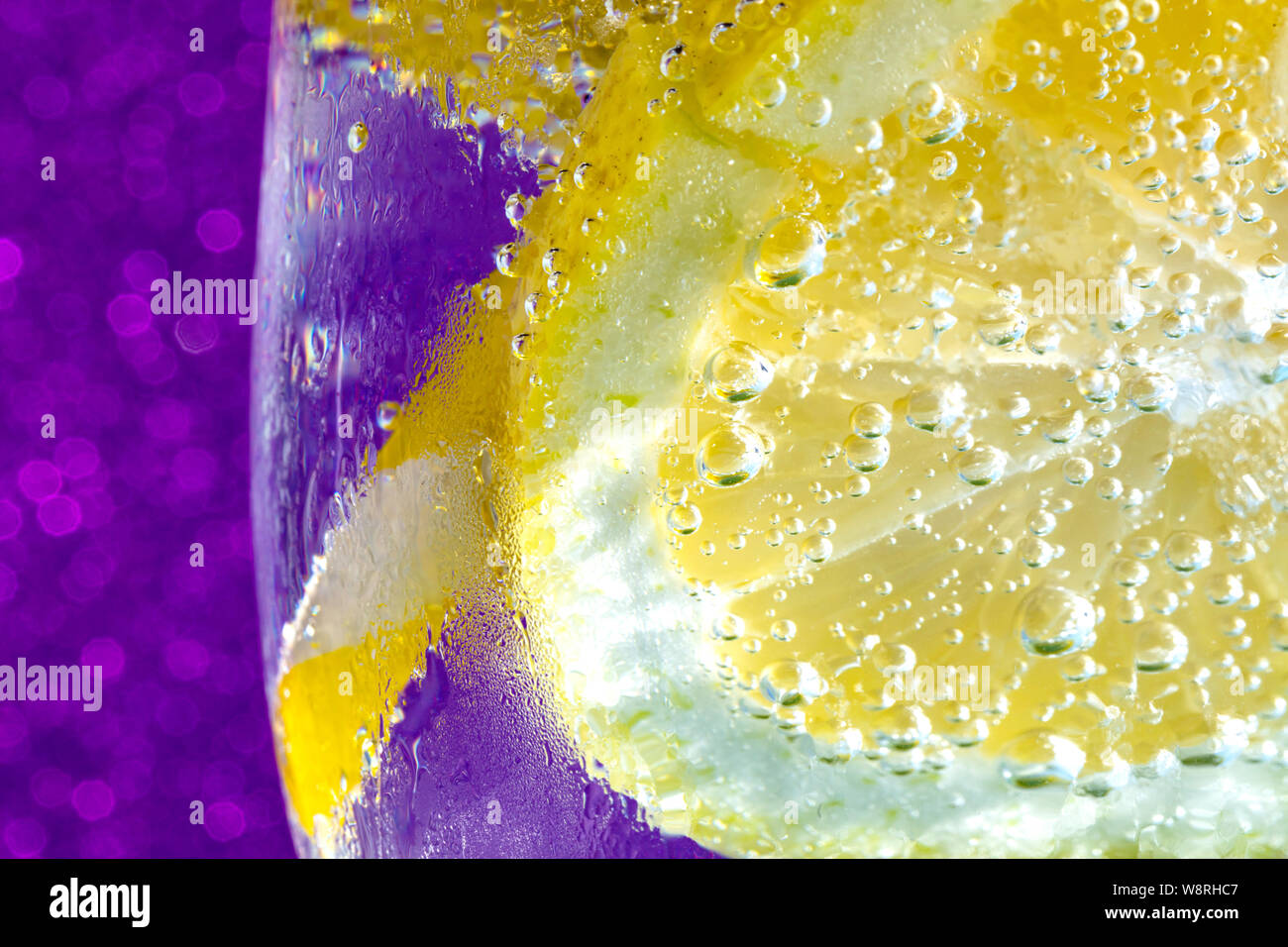 Frisch Soda mit Blasen einen Eiswürfel, einer Scheibe Zitrone und ein Stroh auf eine glänzende lila Hintergrund. Freier Platz für Text Stockfoto