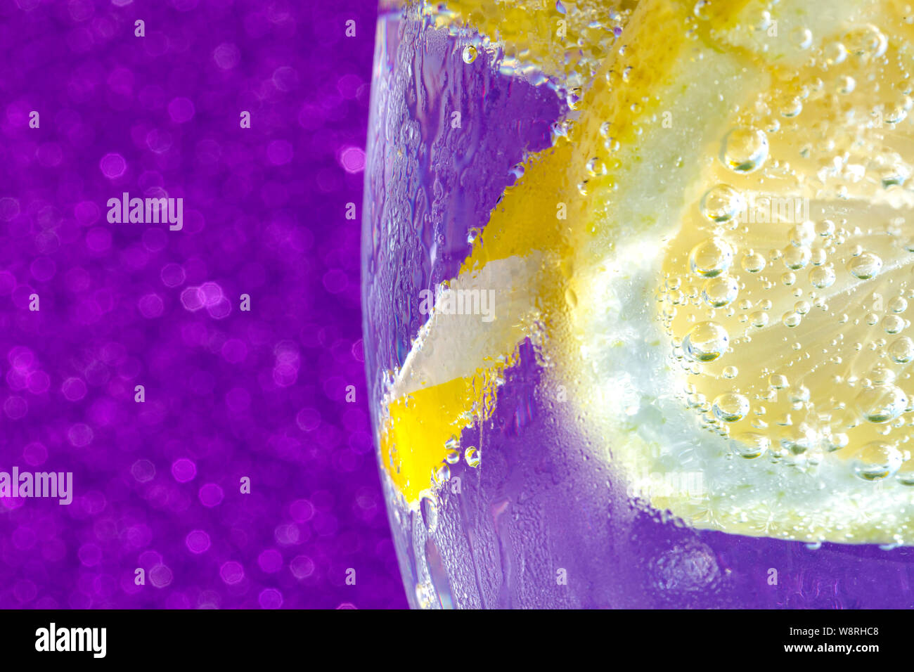 Frisch Soda mit Blasen einen Eiswürfel, einer Scheibe Zitrone und ein Stroh auf eine glänzende lila Hintergrund. Freier Platz für Text Stockfoto