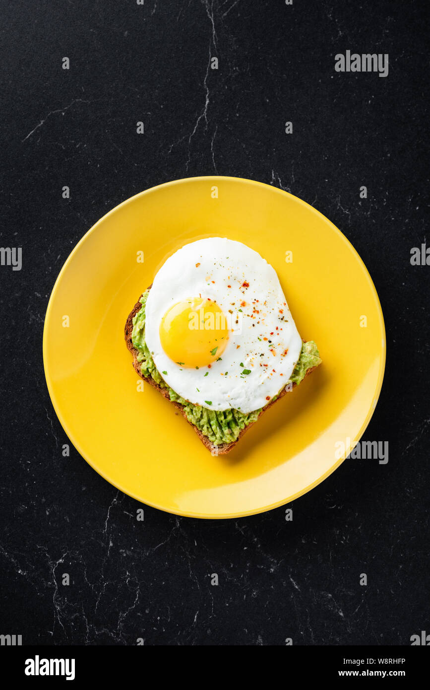 Sunny Side up Ei und Guacamole auf getoastetes Sandwich Brot. Gesundes Frühstück Mittagessen oder einen Snack. Auf gelb, schwarz Marmor tisch Hintergrund, oben Stockfoto