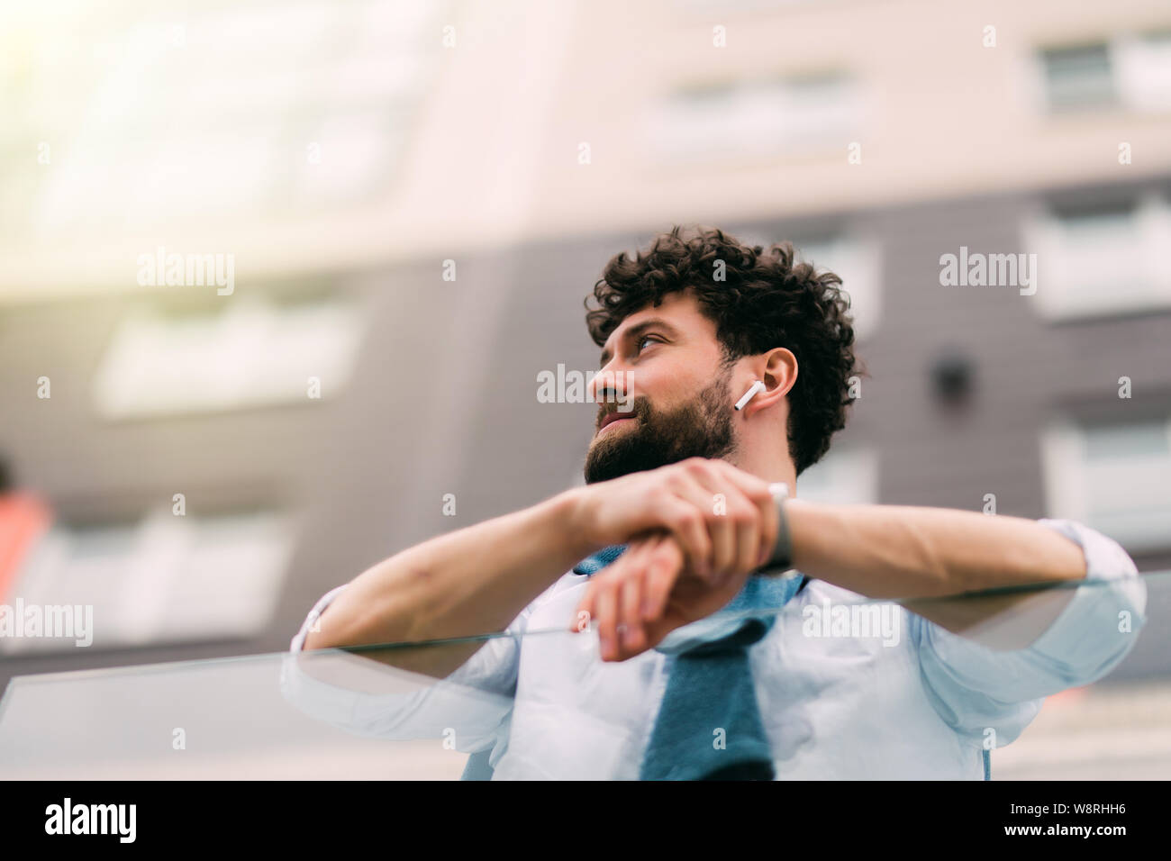 Erfolgreicher Mann in einem blauen Anzug steht in Anlehnung an das Geländer neben modernen Gebäuden, Ruhe im Freien. Weite Einstellung. Stockfoto