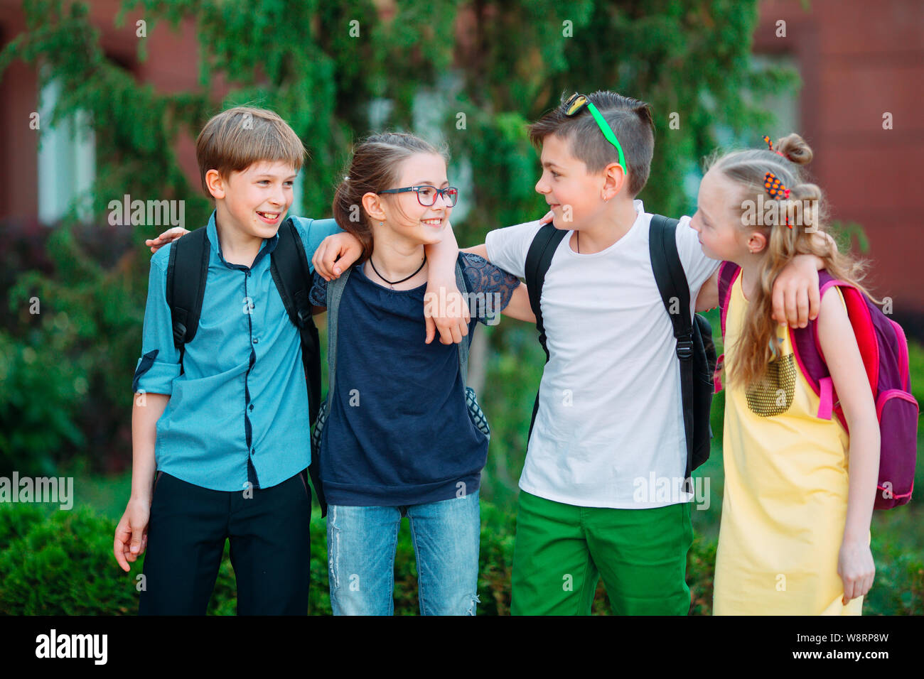 Kinder- Freundschaft. Vier kleine Schüler, zwei Jungen und zwei Mädchen, stand in einer Umarmung auf dem Schulhof. Stockfoto