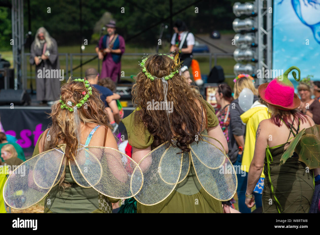 Menschen in ausgefallener Kleidung mit Feenflügeln beim New Forest Fairy Festival, Burley, Ringwood, New Forest, Hampshire, England, Großbritannien als Mutter Ukers Ukulele Band spielen. Stockfoto