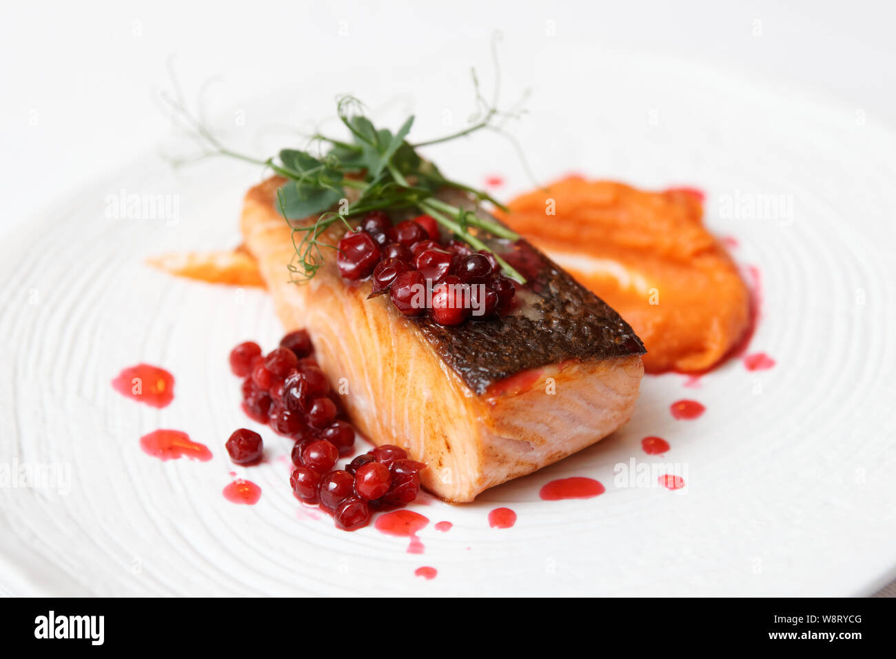 Gebratenes Lachssteak mit kürbispüree, rote Beere Sauce und Kräutern auf weiße Platte Stockfoto